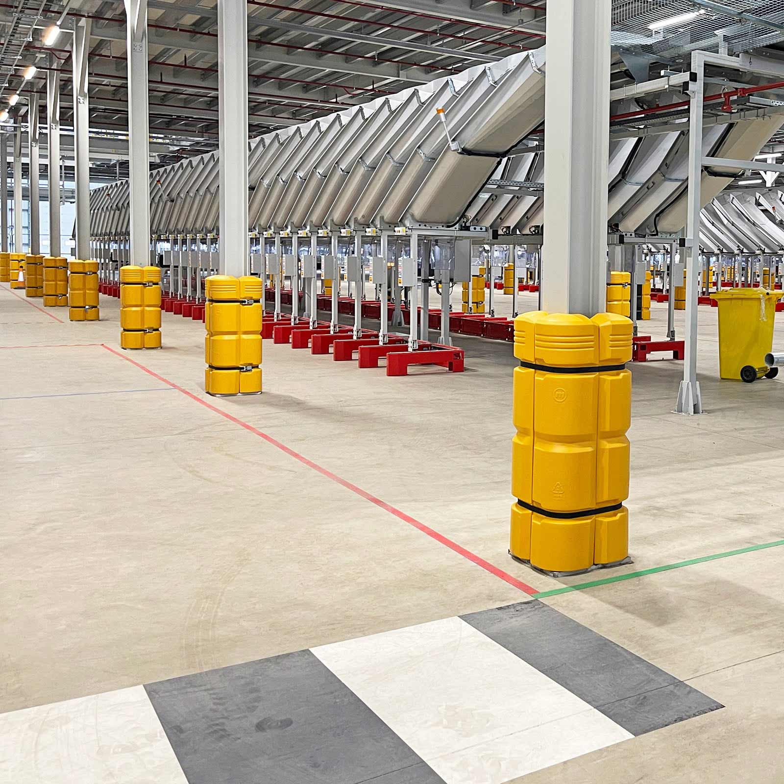 ColumnGuard column guard on a steel column beside a conveyor line and a McCue barrier in a distribution center.
