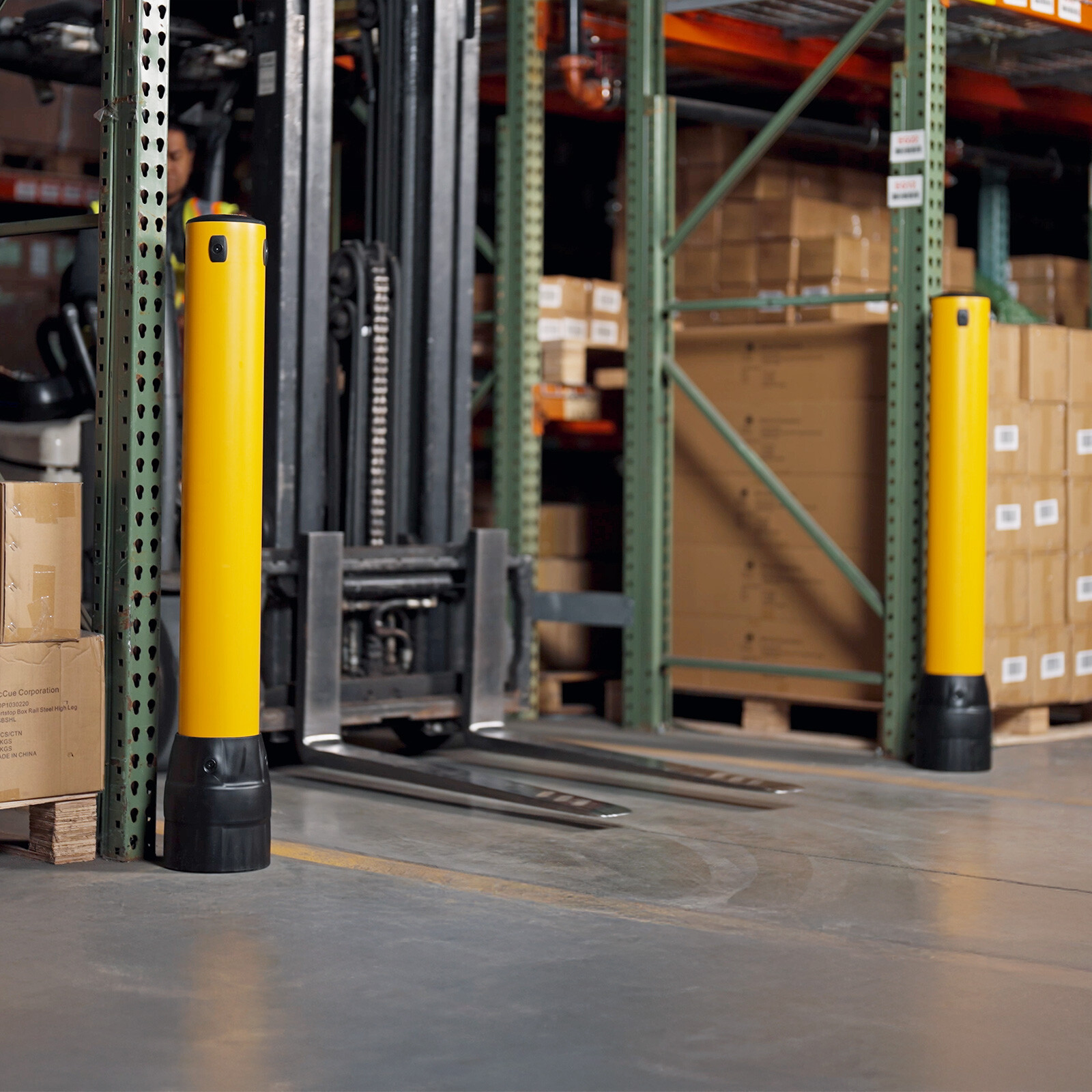 Two FLEX+ Bollards guarding a rack corner as a forklift turns past them in a warehouse aisle.