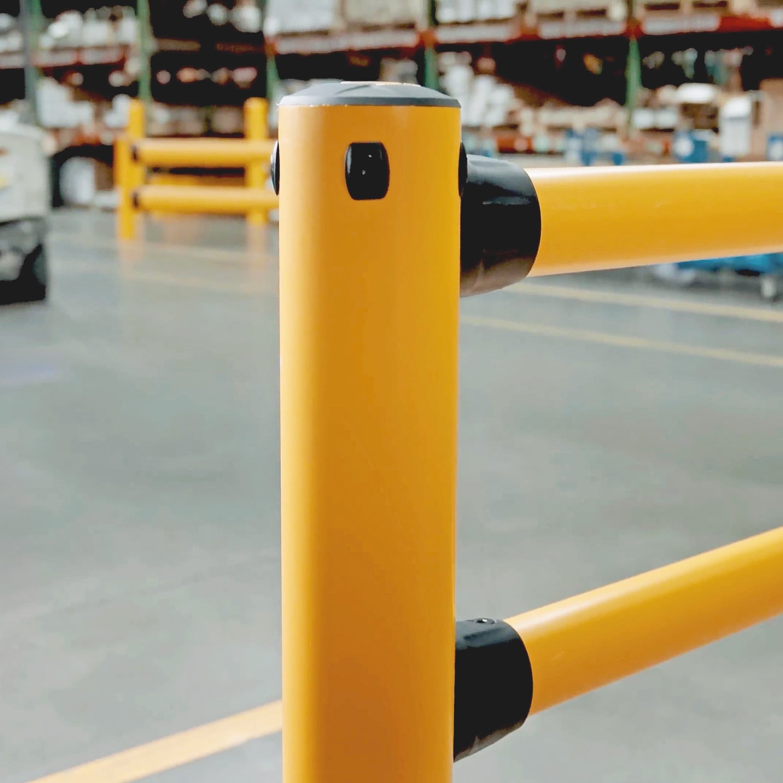 Close-up of a FLEX+ Pedestrian Guard post and its two rail connectors, with warehouse racking behind.