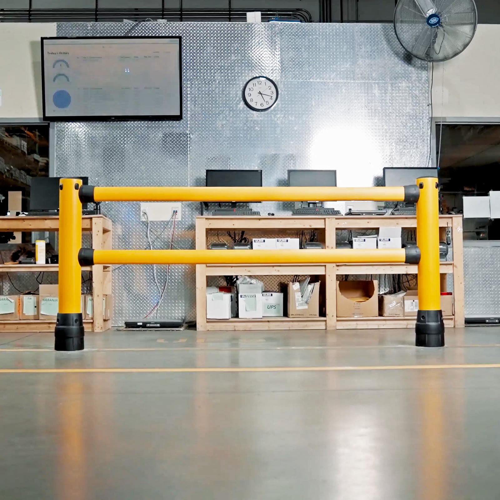 FLEX+ Pedestrian Guard section in front of a warehouse packing station with workbenches and computer monitors.