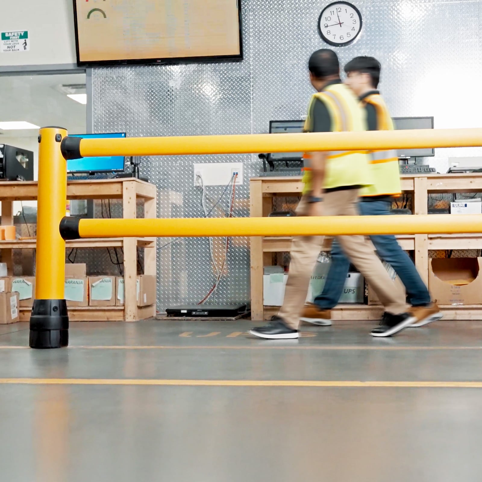 FLEX+ Pedestrian Guard with two workers in safety vests walking behind it at a warehouse packing station.