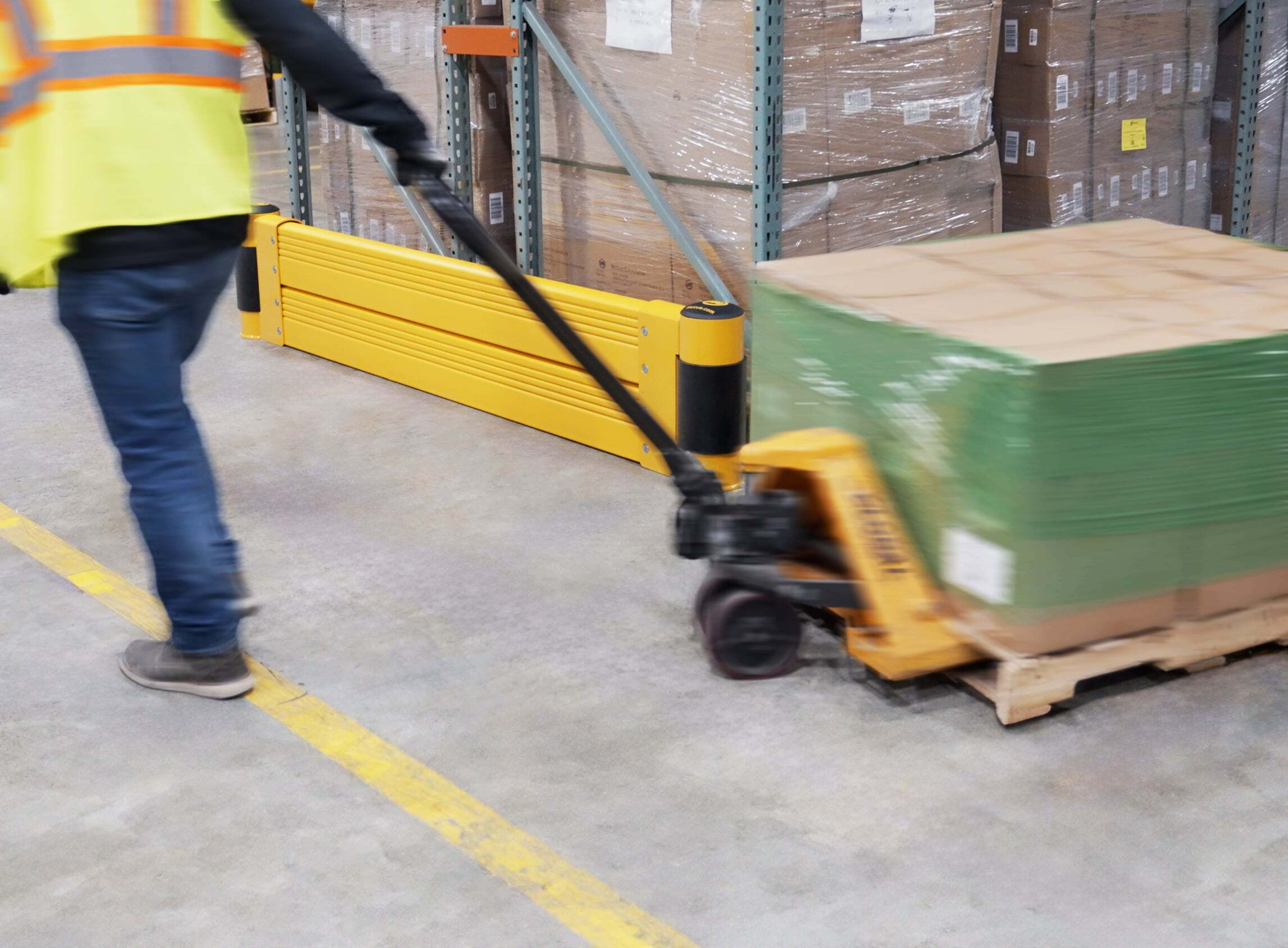 Worker with a loaded pallet jack passing a GroundBarrier Double at a pallet rack end.