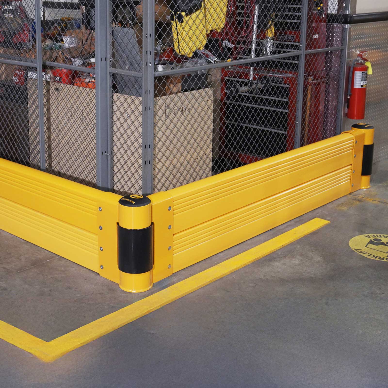 GroundBarrier Double floor-level guardrail wrapped around the corner of a wire-mesh cage in a warehouse.