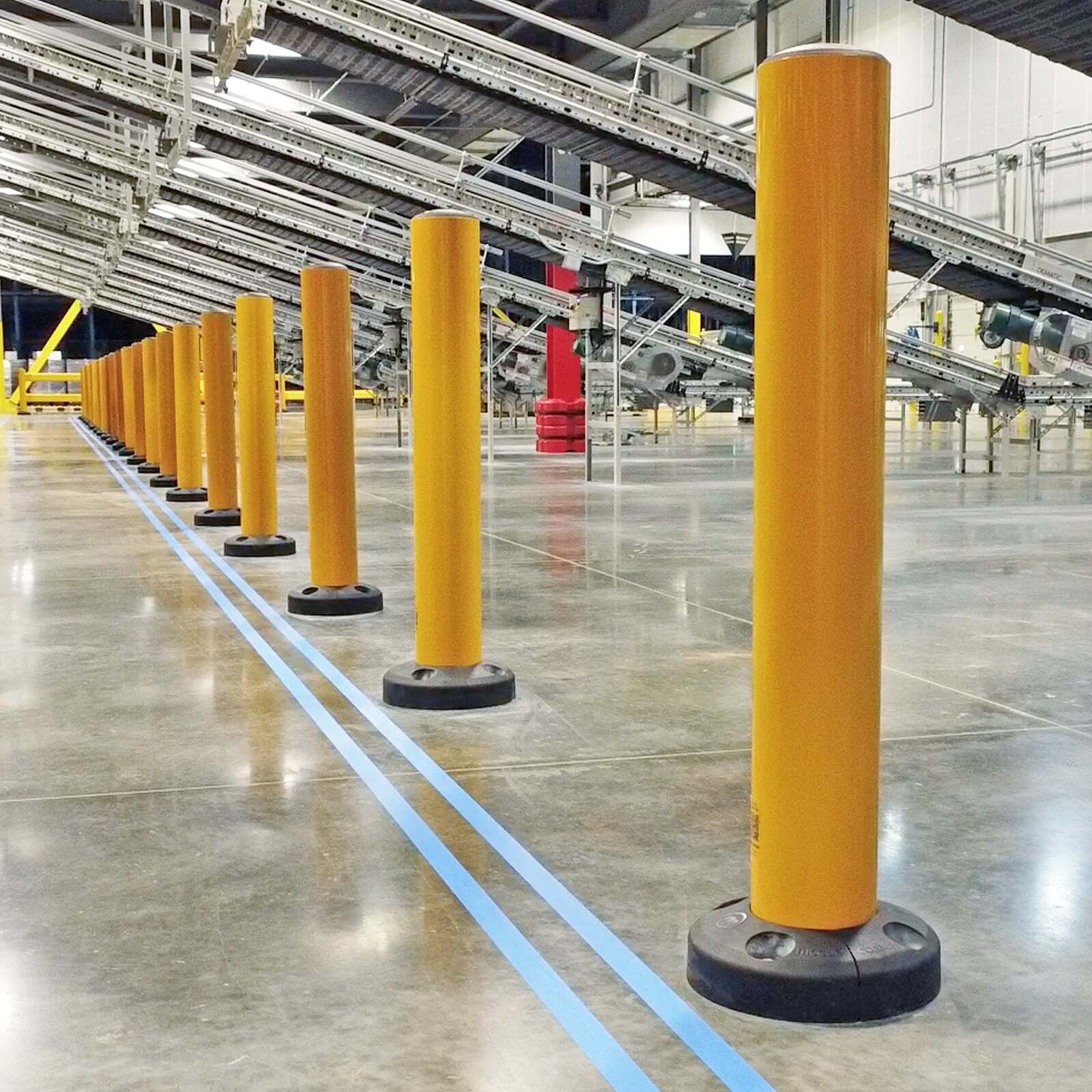 A row of SafeStop Bollard 15 warehouse bollards protecting a conveyor line in a distribution center.
