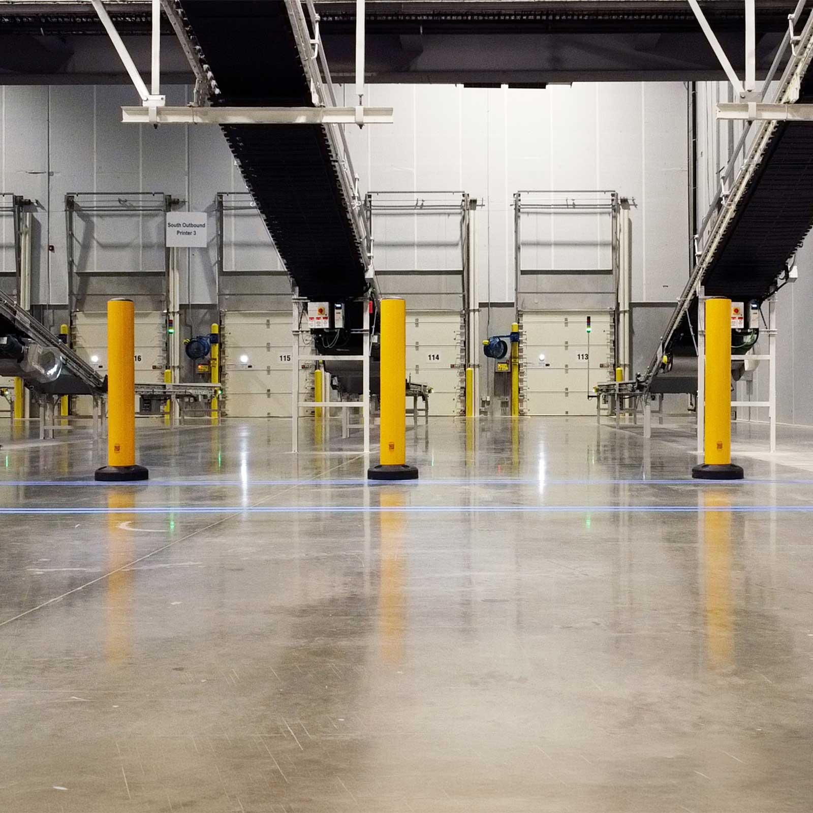 SafeStop Bollard 15 industrial bollards for forklifts guarding a row of dock doors in a distribution center.