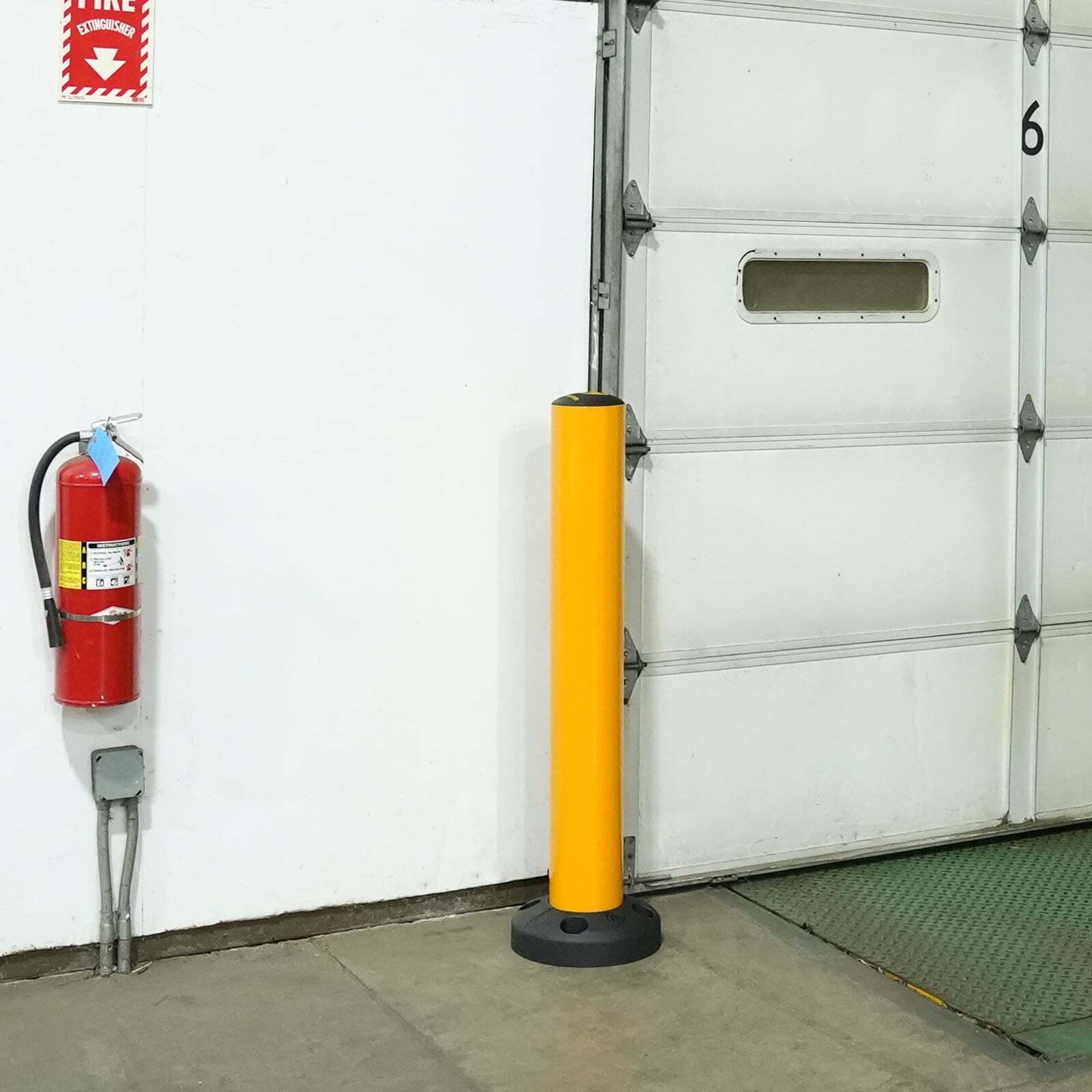 SafeStop Bollard 15 protecting a wall and fire extinguisher beside a dock door in a warehouse.