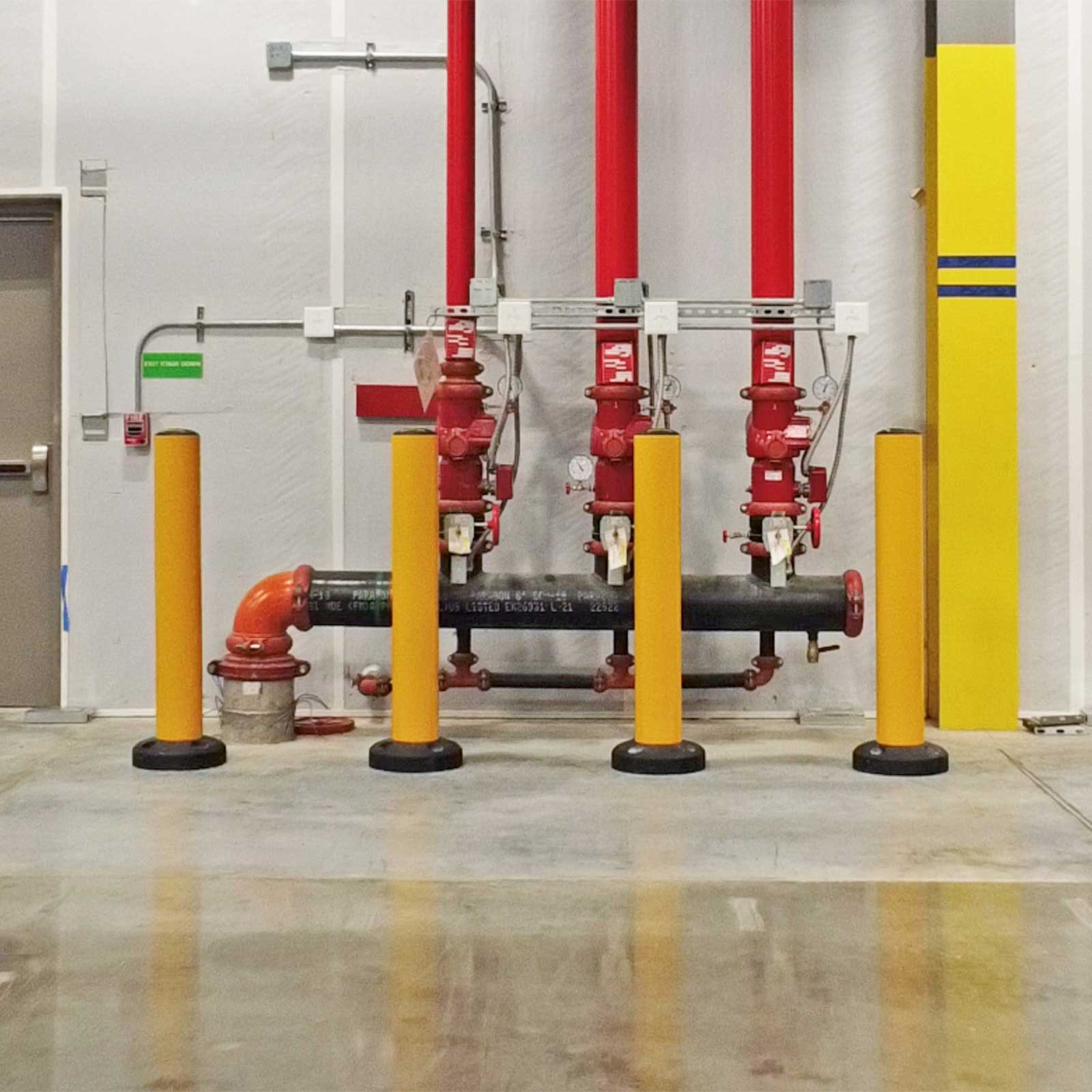Four SafeStop Bollard 15 bollards protecting fire sprinkler risers from forklift impact in a distribution center.