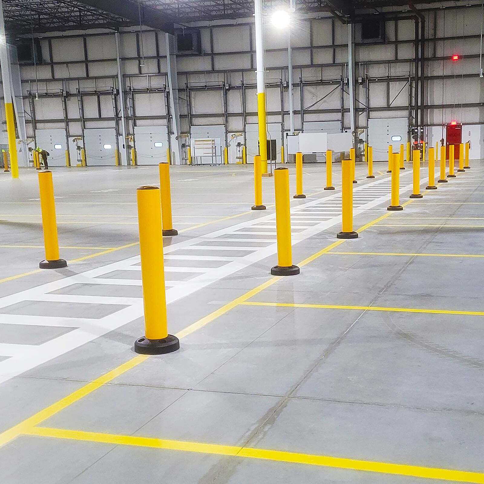 SafeStop Bollard 15 warehouse bollards lining a striped forklift traffic lane in a large warehouse.
