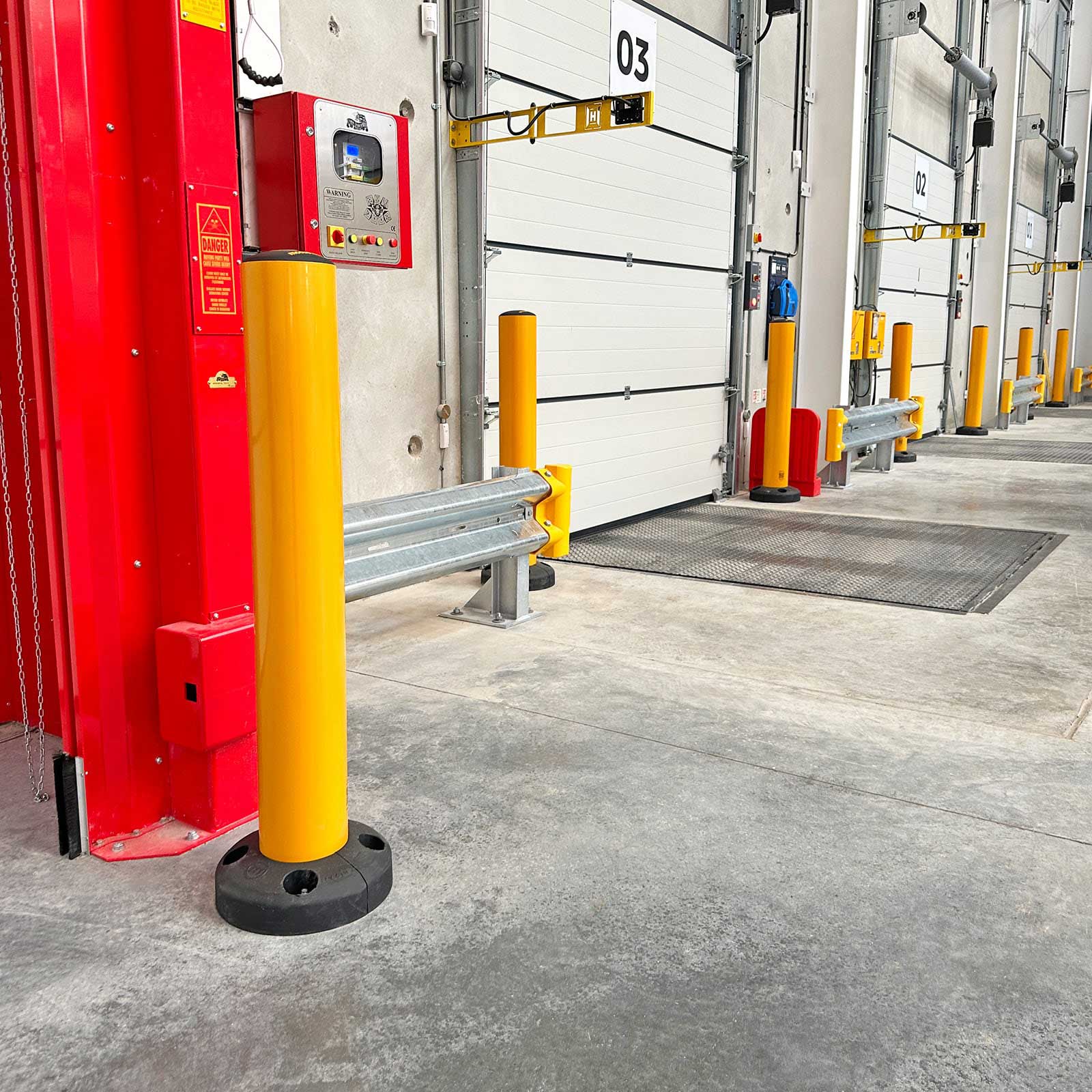 SafeStop Bollard 15 shielding a loading dock door control panel from forklift impact, with a McCue barrier behind it.