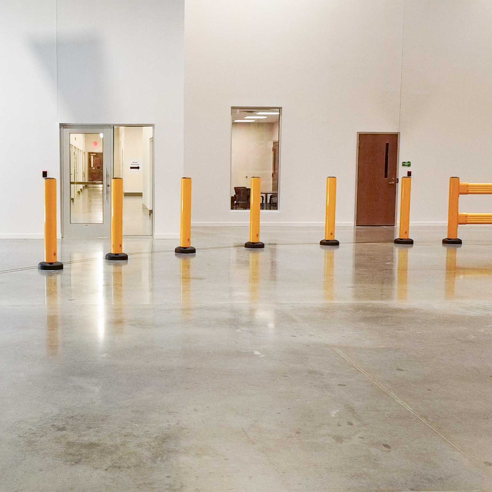 Seven SafeStop Bollard 15 bollards and a SafeStop GuardRail shielding office doors and a window from forklift traffic.