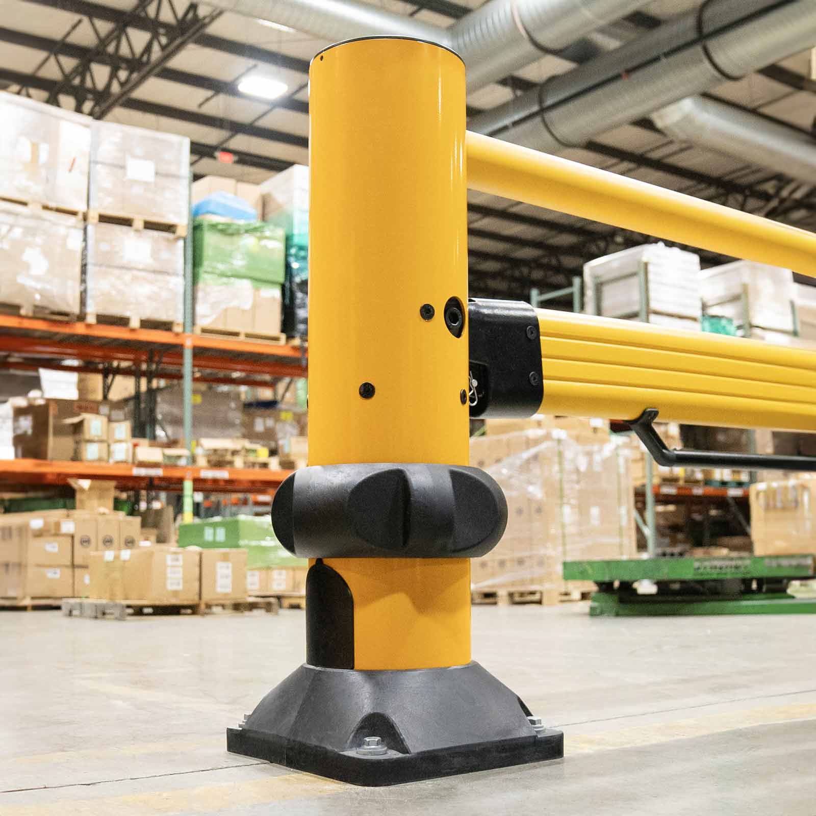Close-up of the SafeStop ForkLift Gate post, elastomer base, and rail bracket in front of loaded pallet racking.