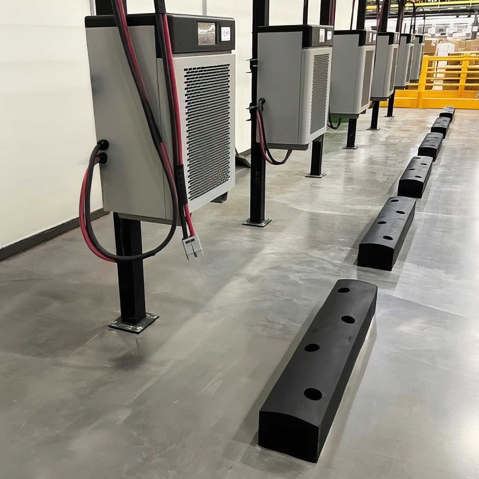 SafeStop ForkShield barriers protecting a row of battery chargers on floor stands from forklift impacts in a warehouse.