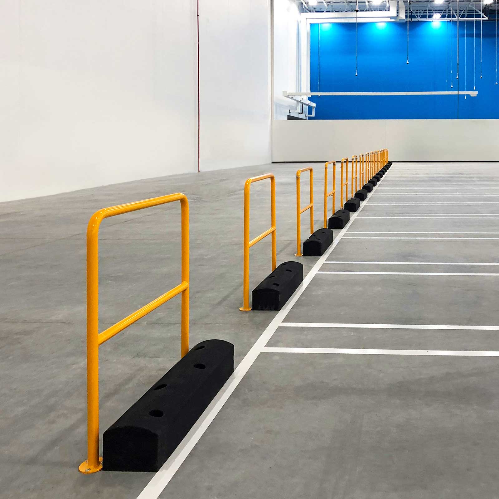 A row of SafeStop ForkShield low-level forklift barriers lining equipment parking stalls in a warehouse.