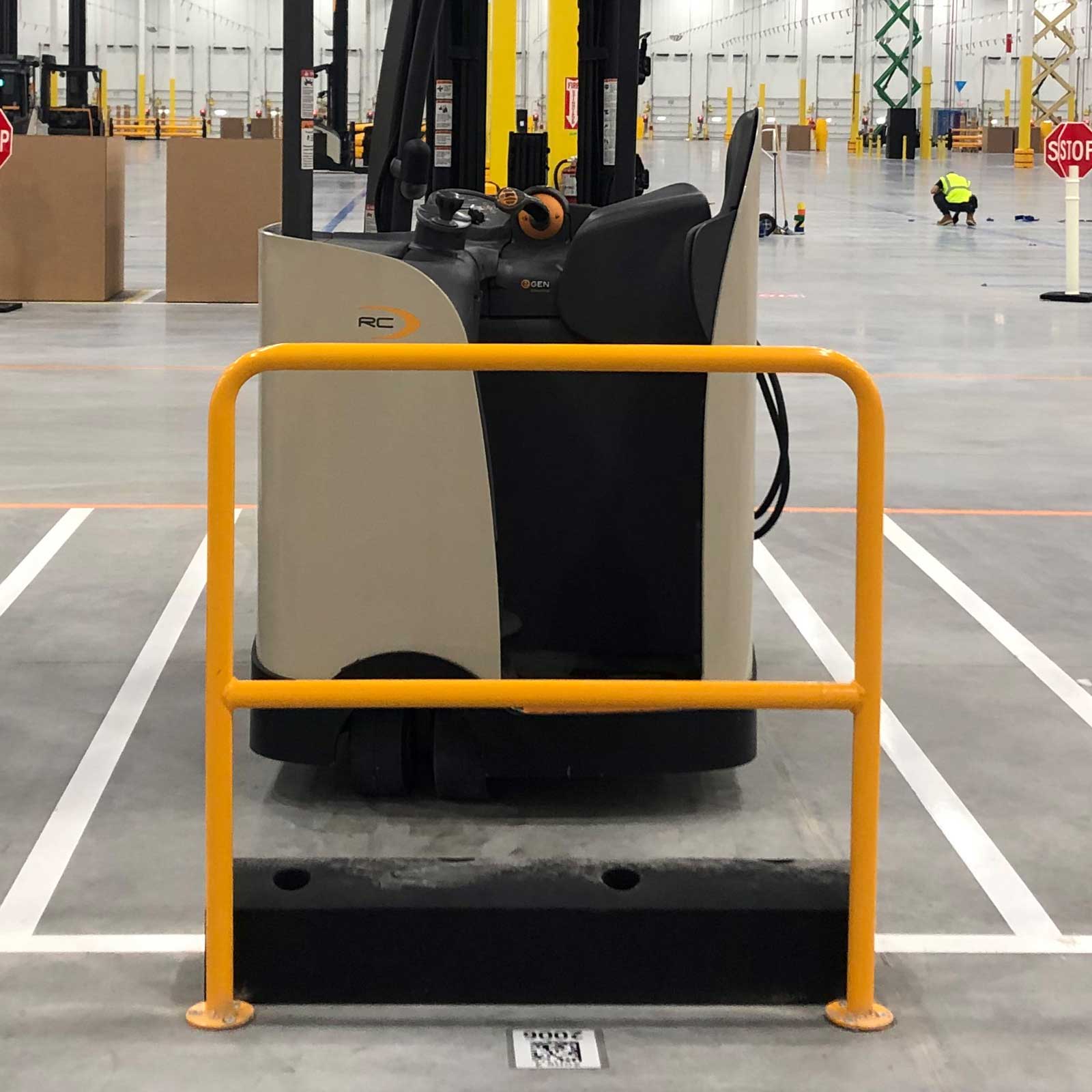 A SafeStop ForkShield shock-absorbing barrier stopping a parked material handling vehicle short of a yellow guardrail.