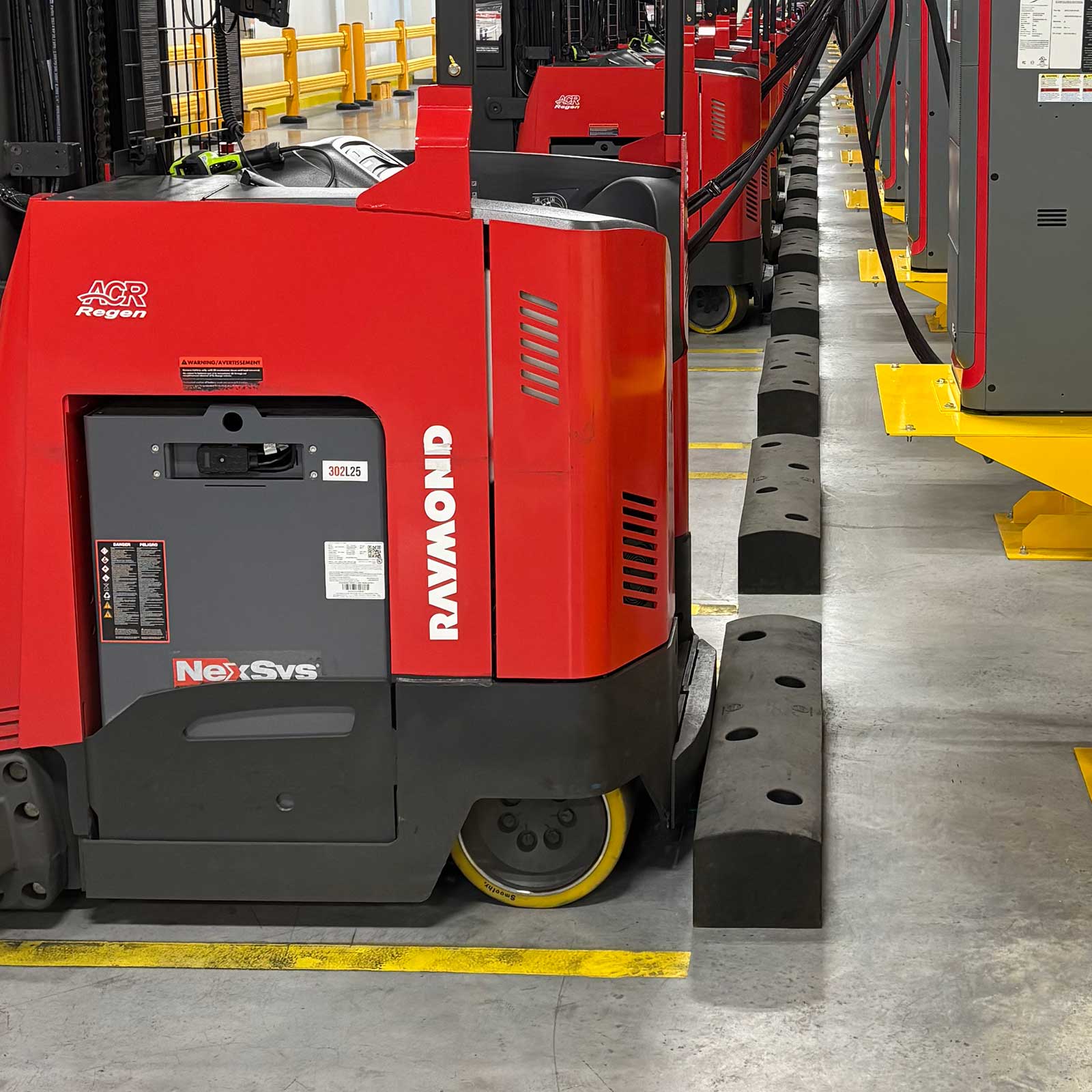 A run of SafeStop ForkShield barriers stopping parked reach trucks at a forklift charging area in a distribution center.