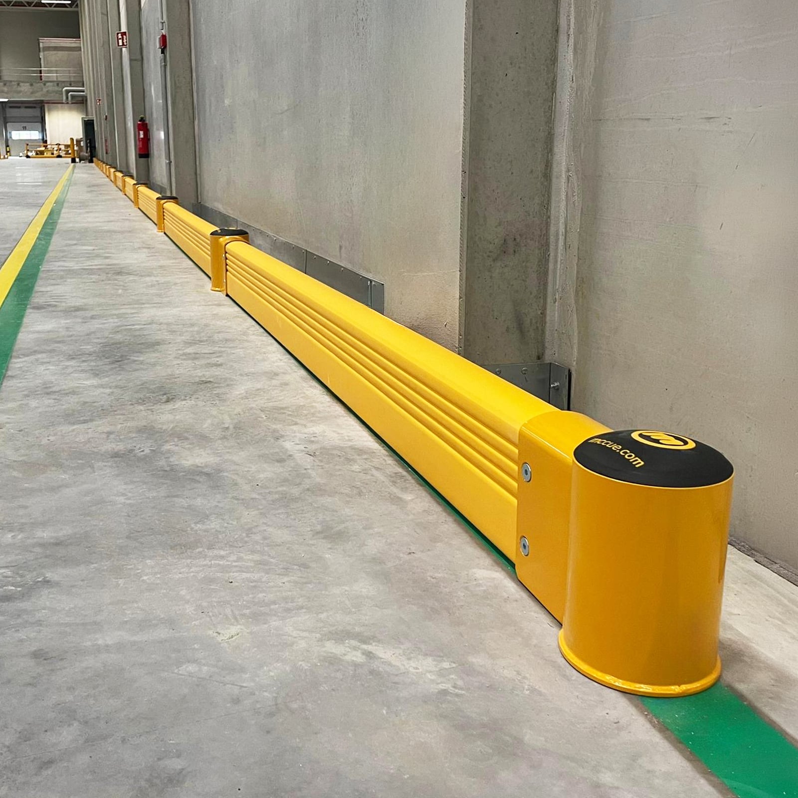 SafeStop GroundBarrier ground-level warehouse barrier along the base of a long concrete wall in a warehouse.