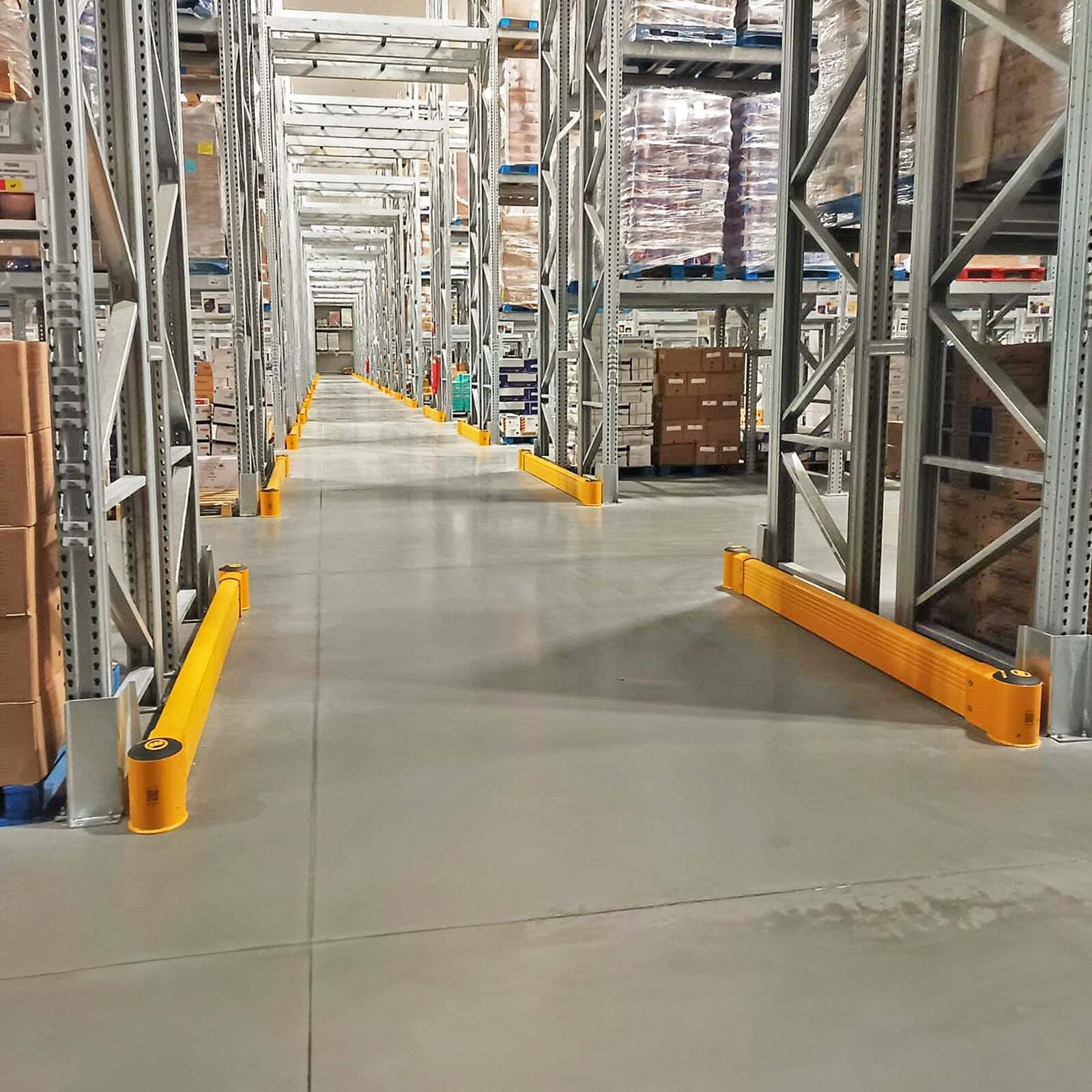 SafeStop GroundBarrier runs at the base of pallet racking on both sides of a long distribution center aisle.