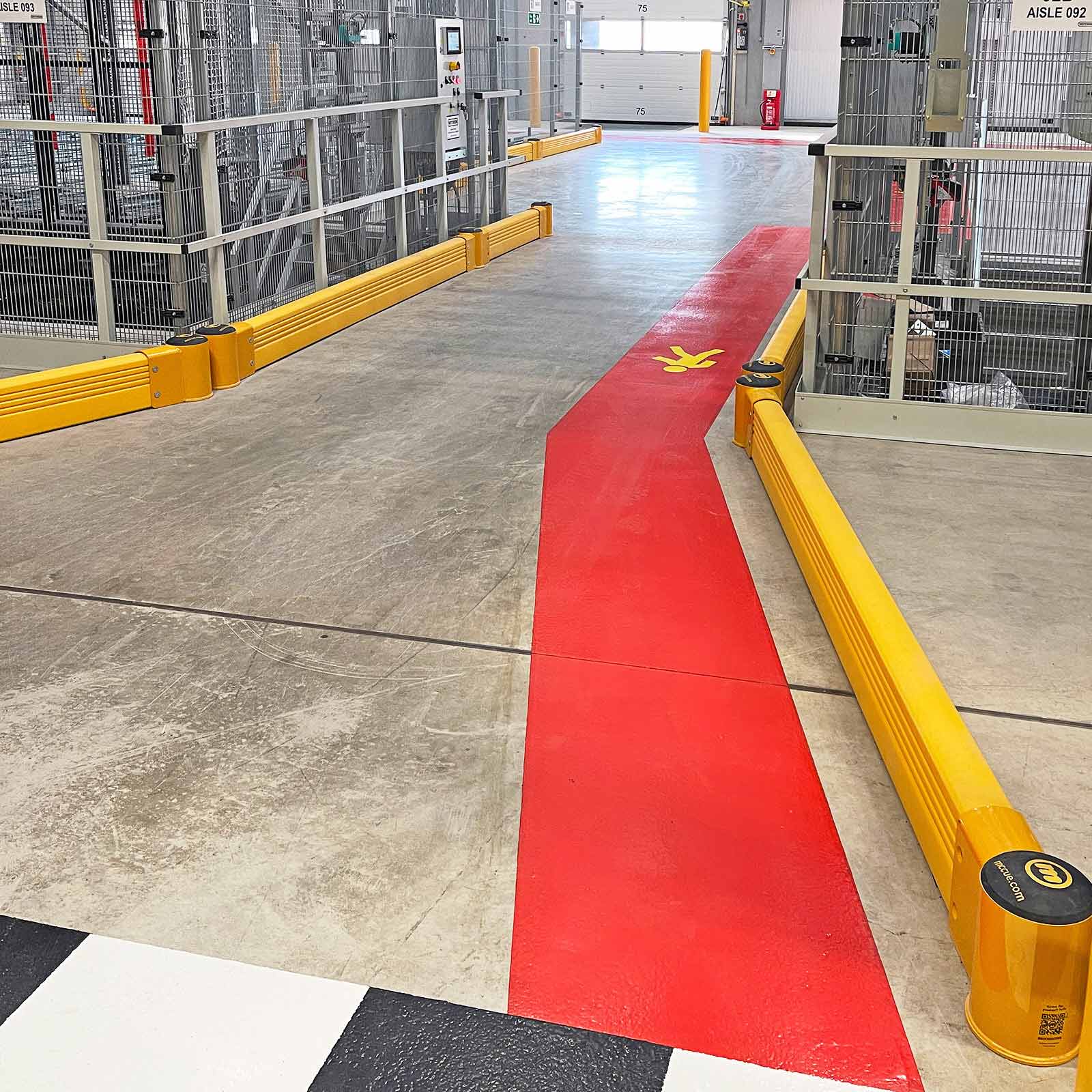 SafeStop GroundBarrier ground-level warehouse barrier lining both sides of a red walkway between wire-mesh storage cages.