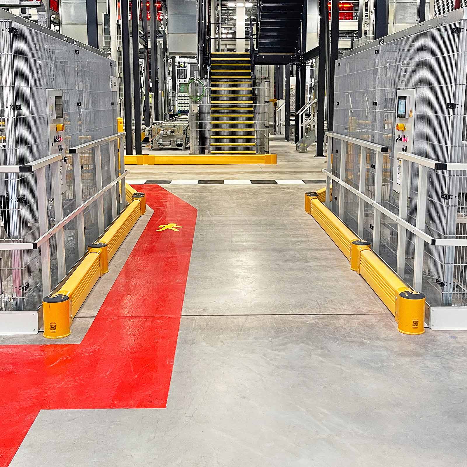 SafeStop GroundBarrier runs along the base of wire-mesh machine guarding on both sides of an aisle beside a red walkway.
