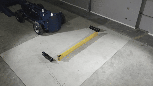 Impact test of a SafeStop GroundBarrier as a blue test vehicle strikes a short run on a concrete floor.