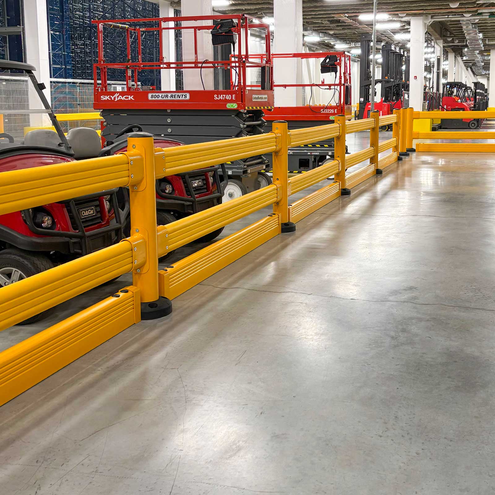 SafeStop GuardRail forklift impact barriers with FloorGuard separating parked utility carts and scissor lifts from an aisle.