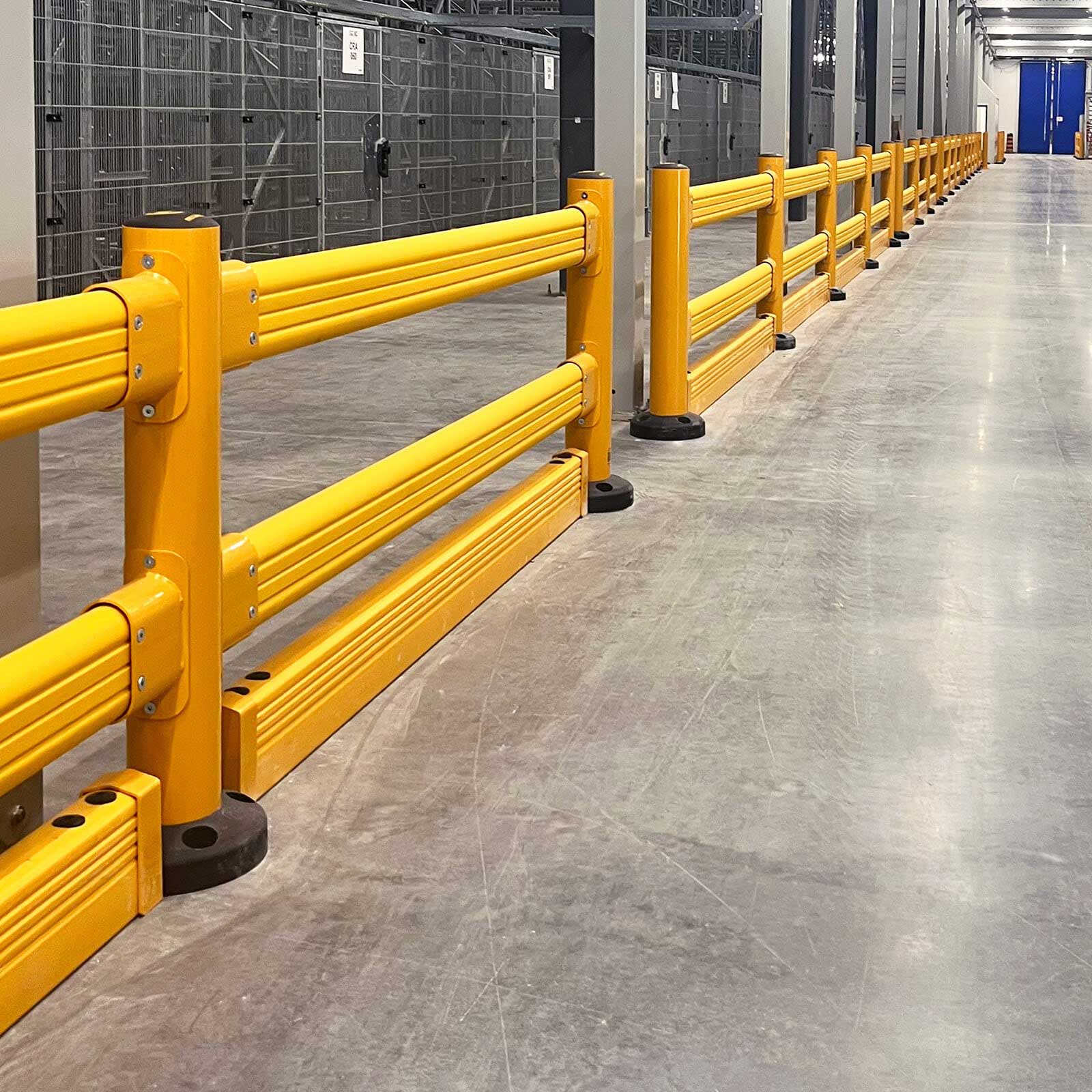SafeStop GuardRail forklift impact barriers with FloorGuard lining a long warehouse aisle beside storage cages.