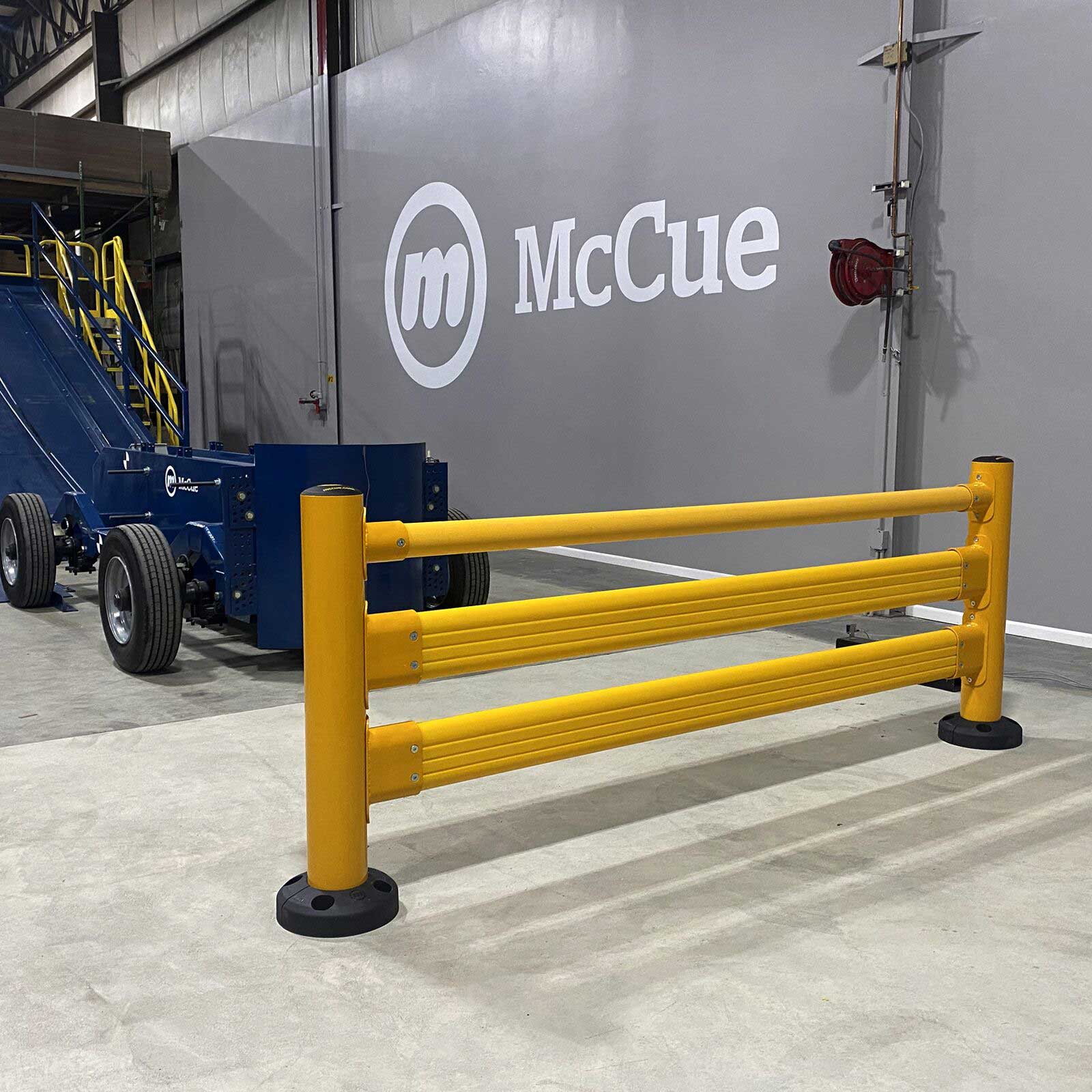 SafeStop Pedestrian GuardRail section in front of a McCue logo wall, with a blue McCue test cart beside it.