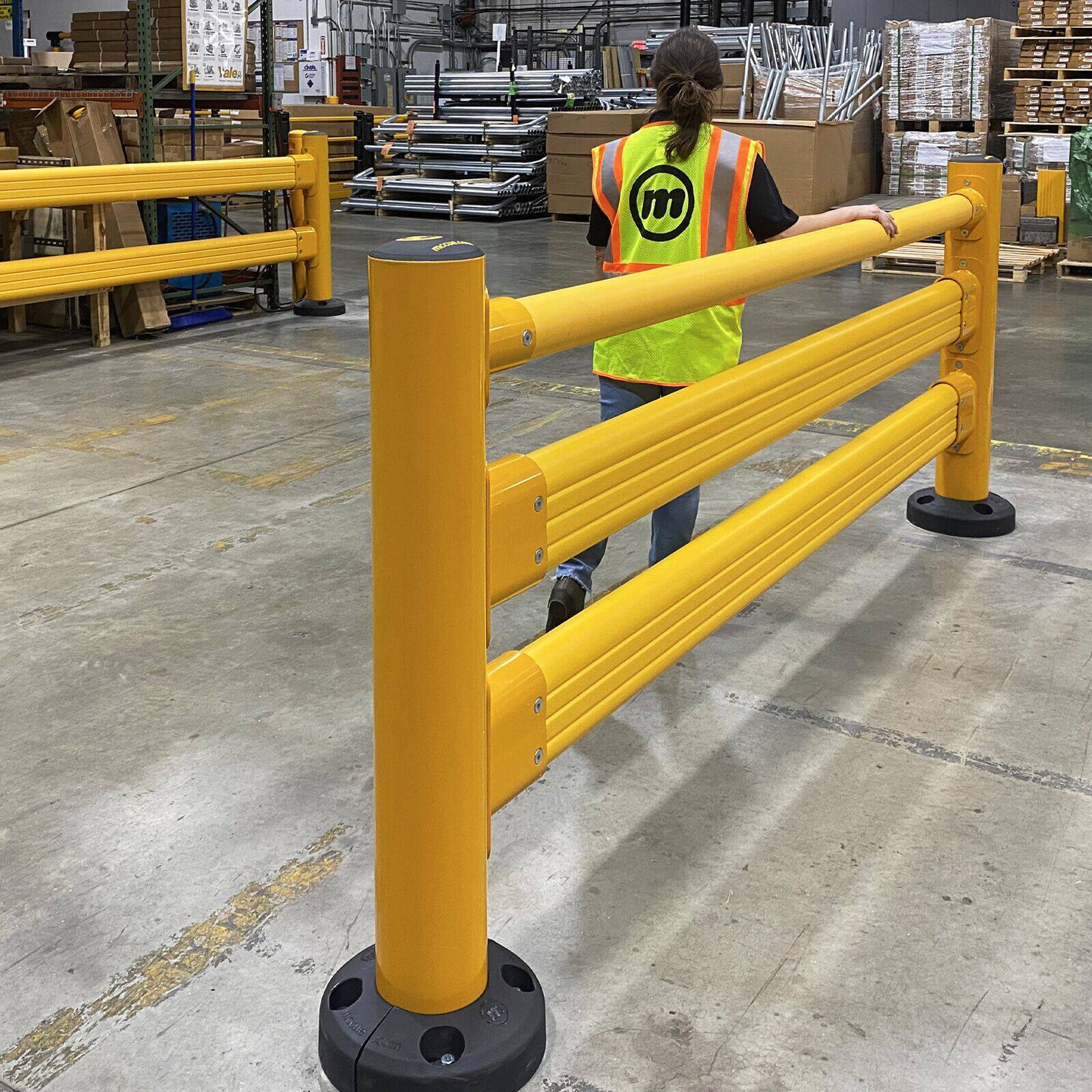Worker in a high-visibility vest walking along SafeStop Pedestrian GuardRail with a hand on its top handrail.