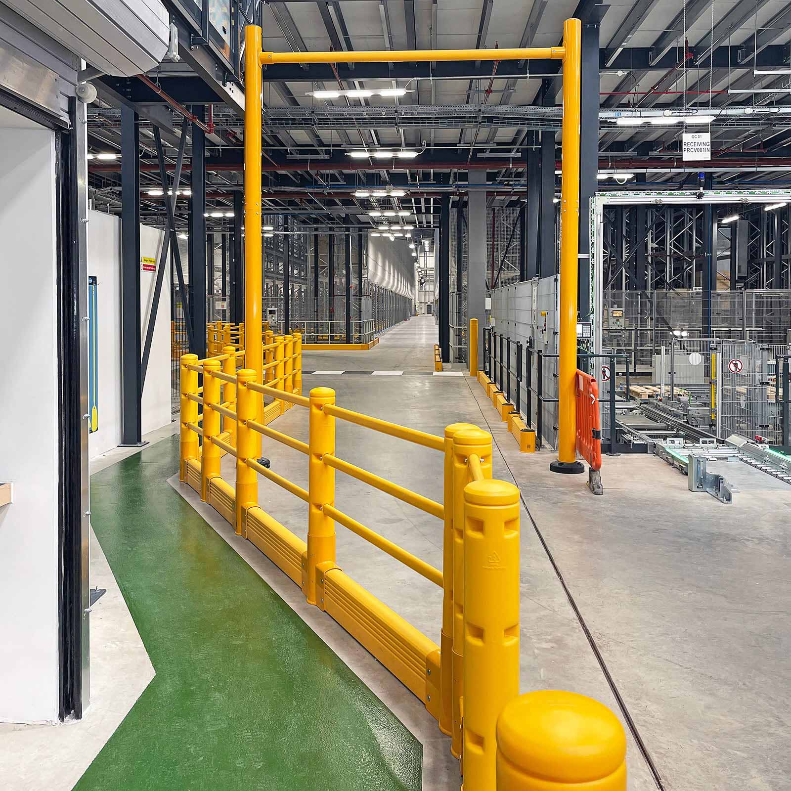 SafeStop Pedestrian with GroundBarrier lining a green pedestrian walkway that runs under a SafeStop GoalPost in a warehouse.