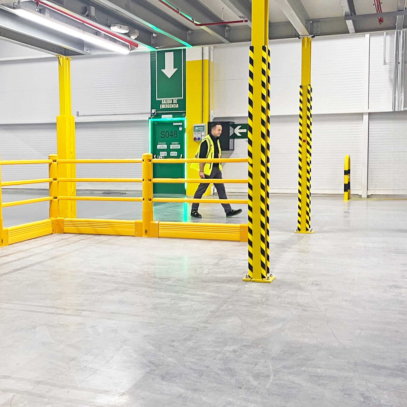 Worker in a safety vest walking behind a SafeStop Pedestrian with GroundBarrier near a fire exit in a warehouse.