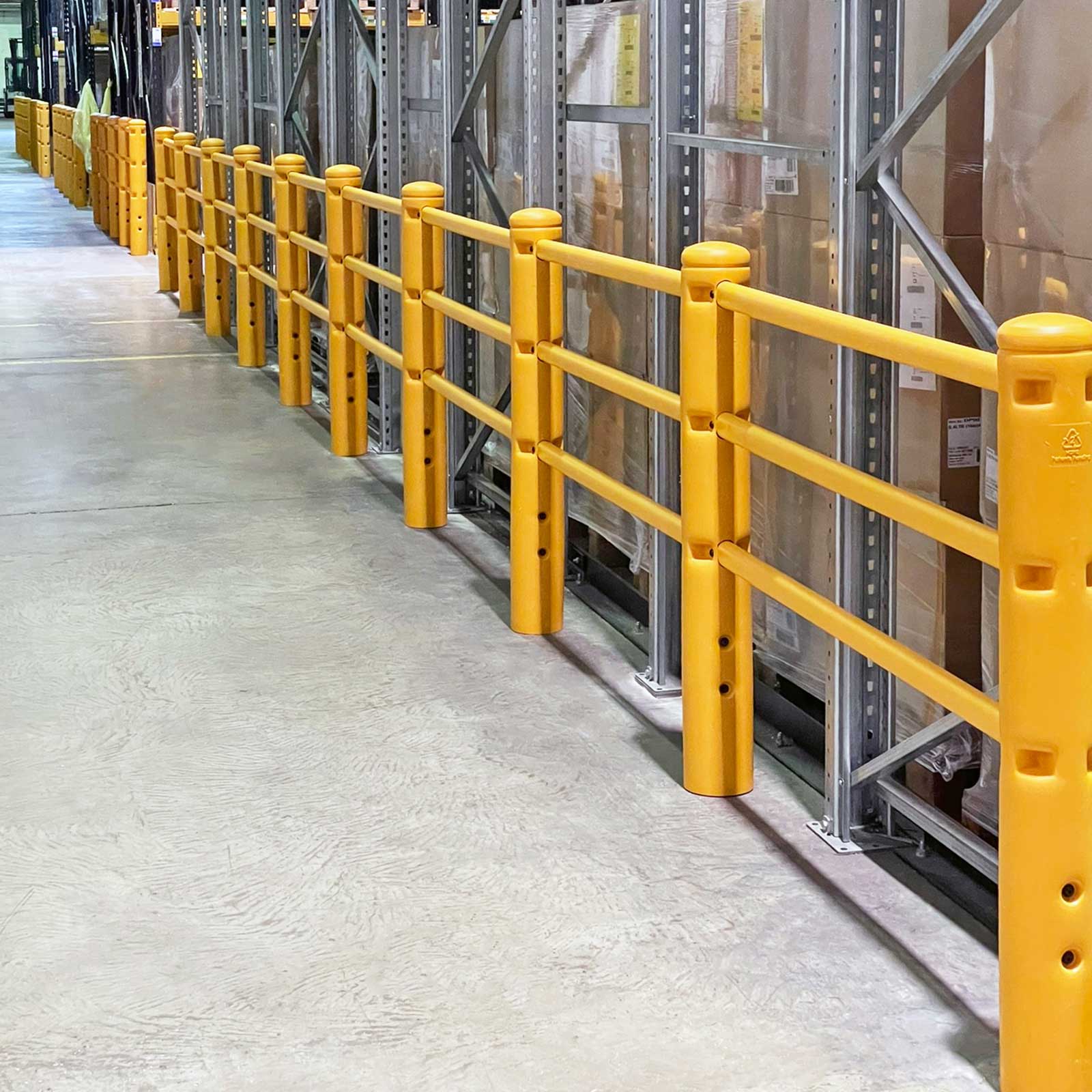 Long run of SafeStop PedestrianBarrier lining a warehouse aisle beside stocked racking.