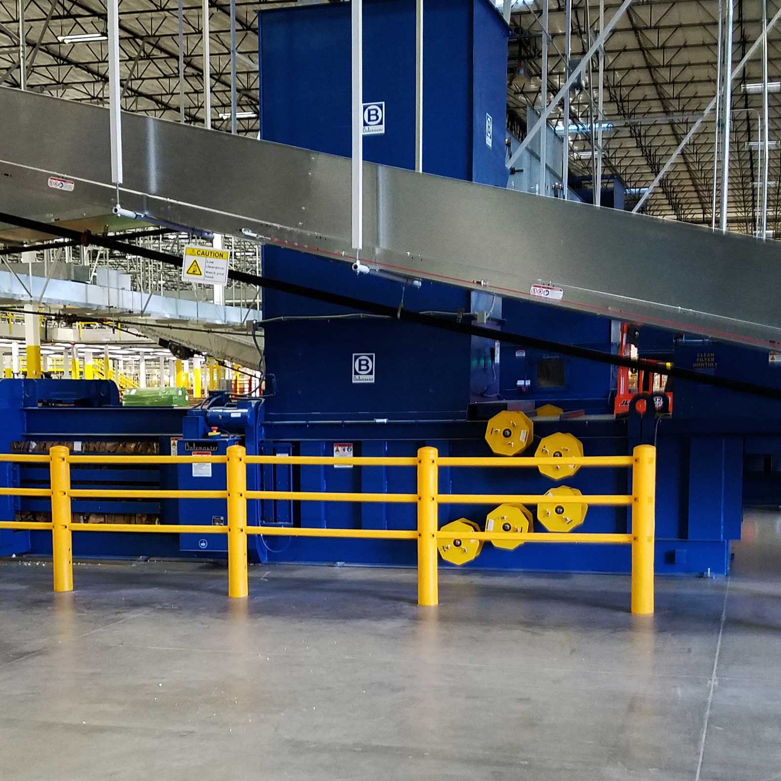 SafeStop PedestrianBarrier along blue processing equipment under an overhead conveyor in a distribution center.