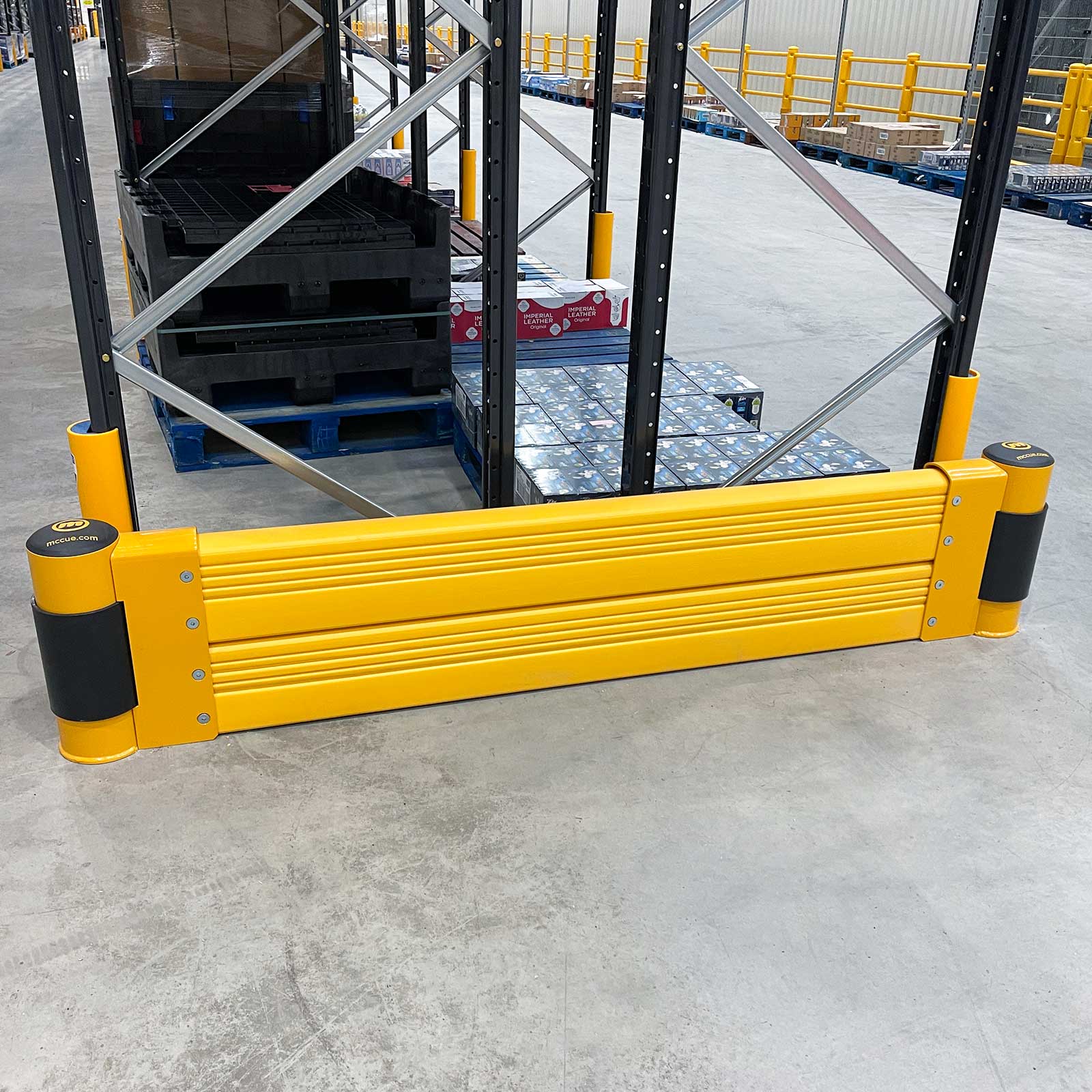 SafeStop RackEnd Protector Double across the end of a black pallet rack stocked with boxed goods in a warehouse.