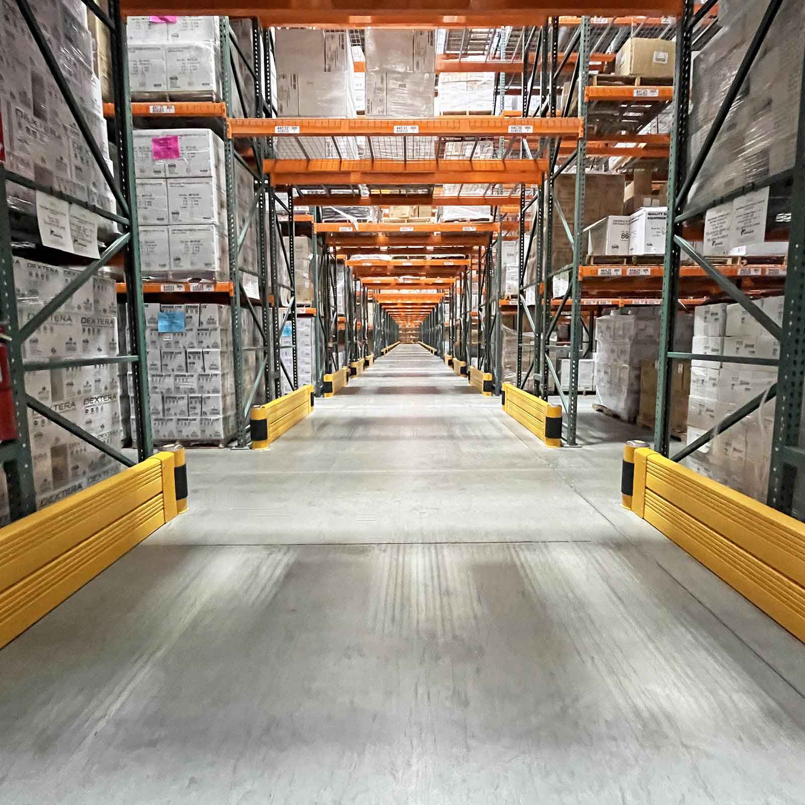 SafeStop RackEnd Protector Double units on pallet rack ends along both sides of a long distribution center aisle.