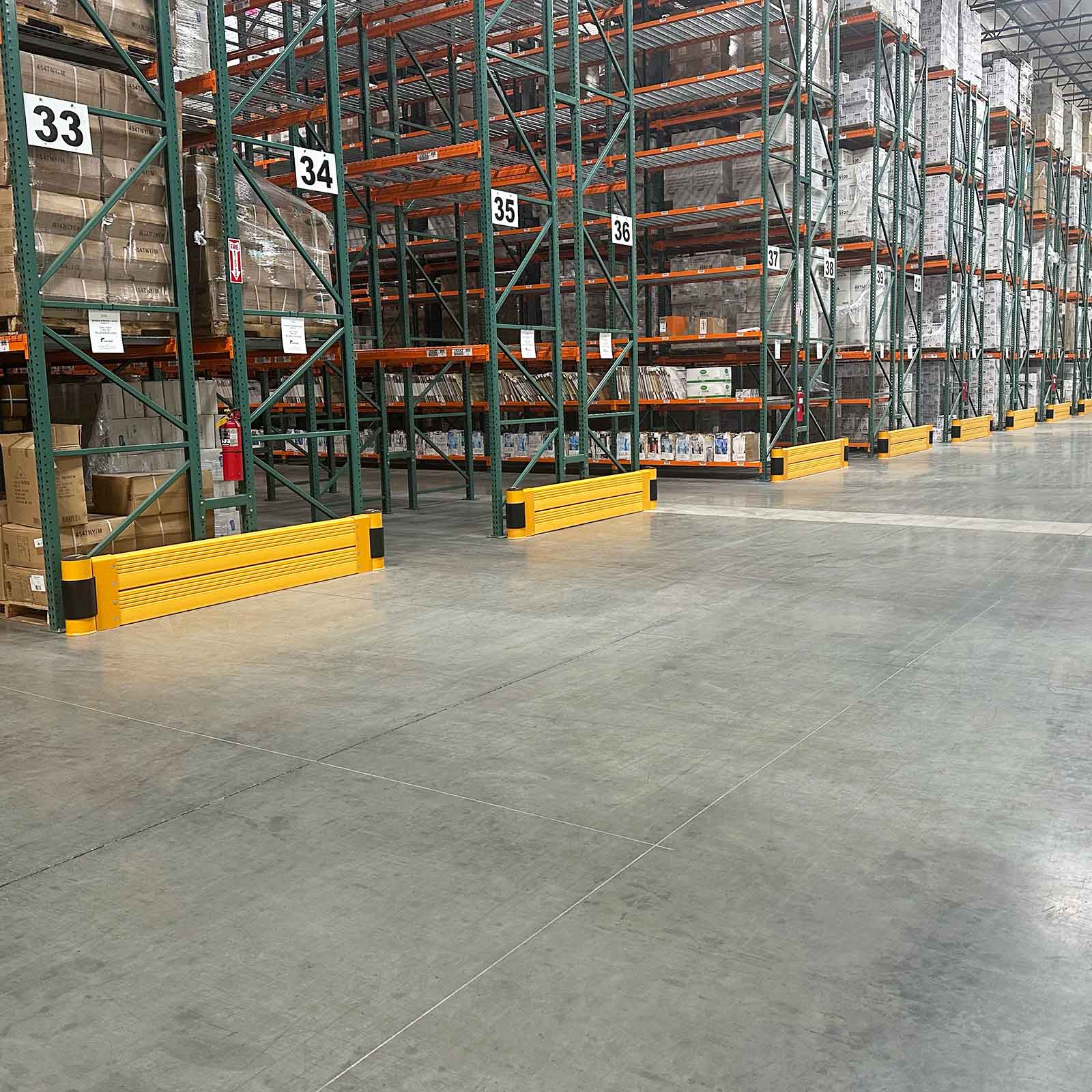 SafeStop RackEnd Protector Double units on a row of numbered pallet rack ends along a wide distribution center aisle.