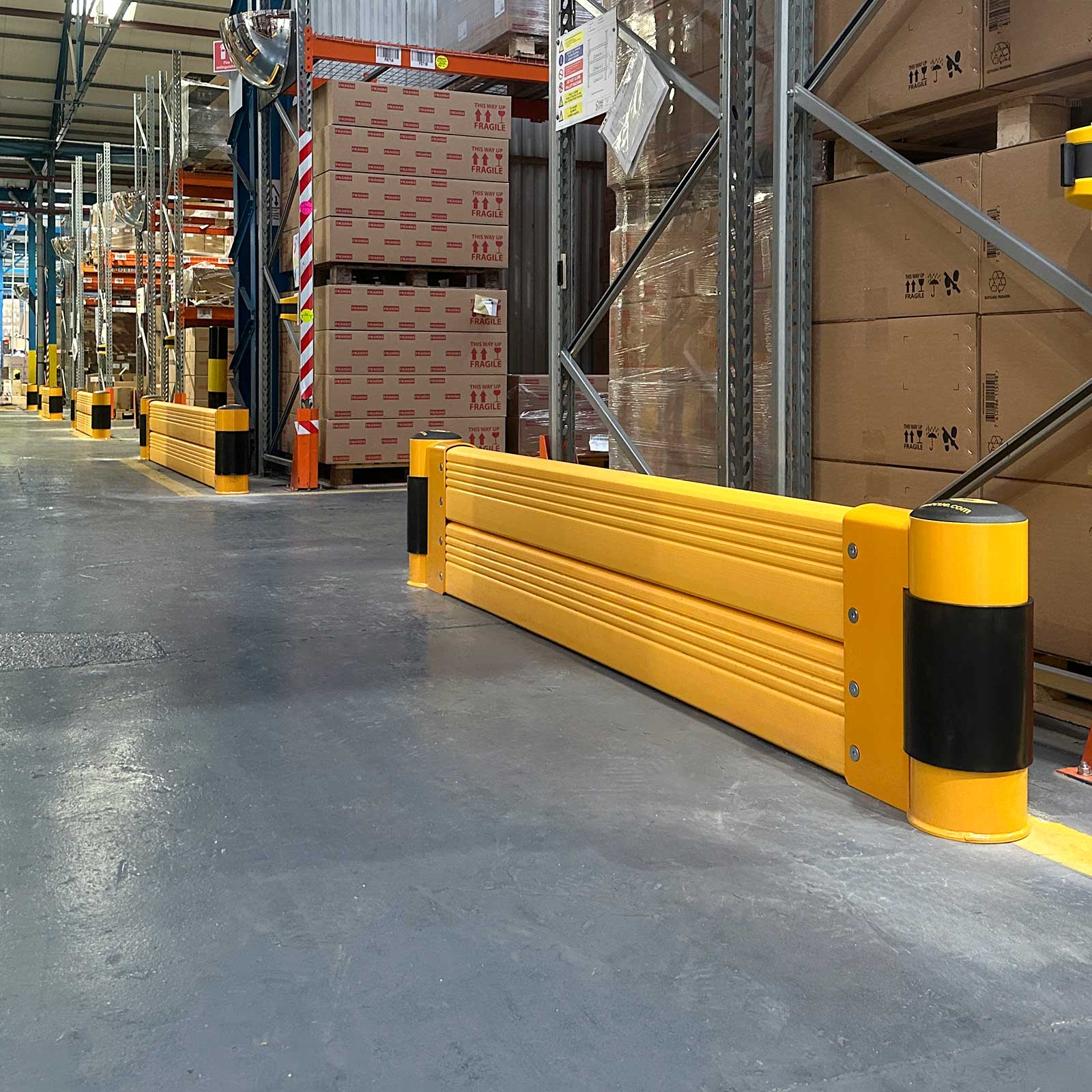 SafeStop RackEnd Protector Double at a pallet rack end stacked with cartons, with more units down a warehouse aisle.