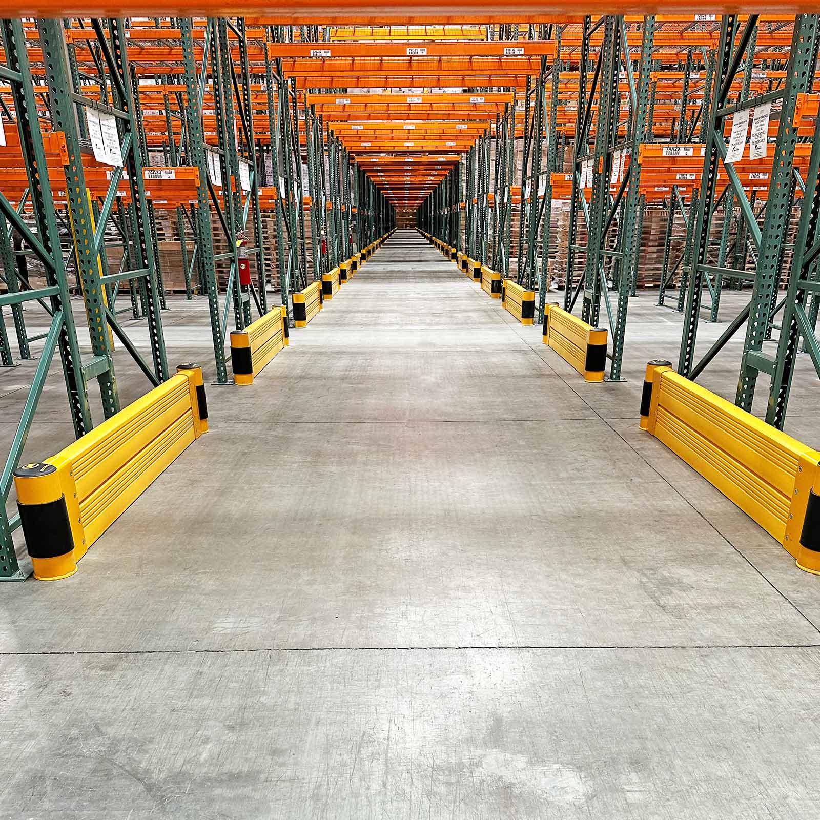 SafeStop RackEnd Protector Double units on both sides of a narrow aisle between orange and green pallet racks.