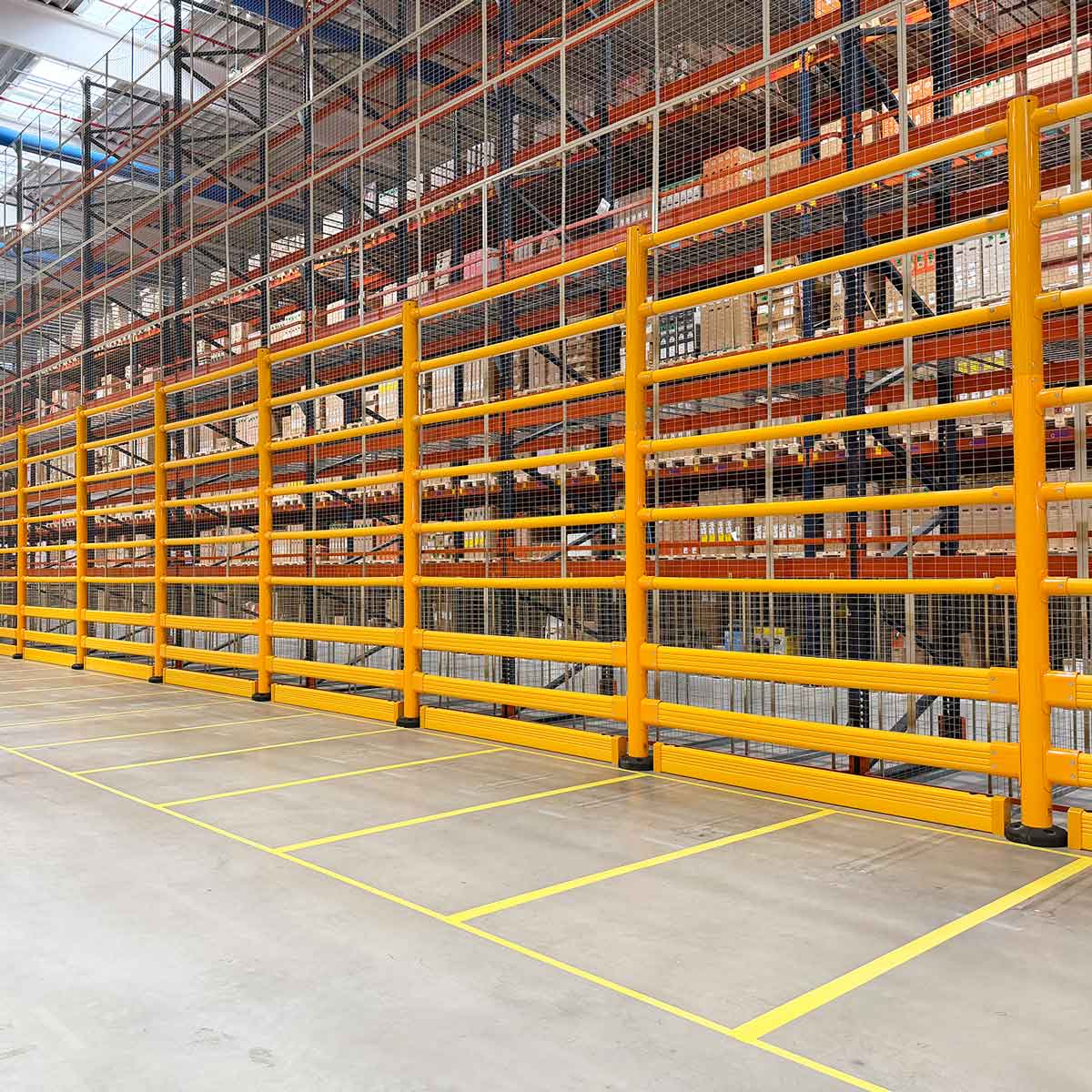 A long run of SafeStop ToppleBarrier 176 protecting mesh-backed pallet racking along a forklift aisle in a warehouse.