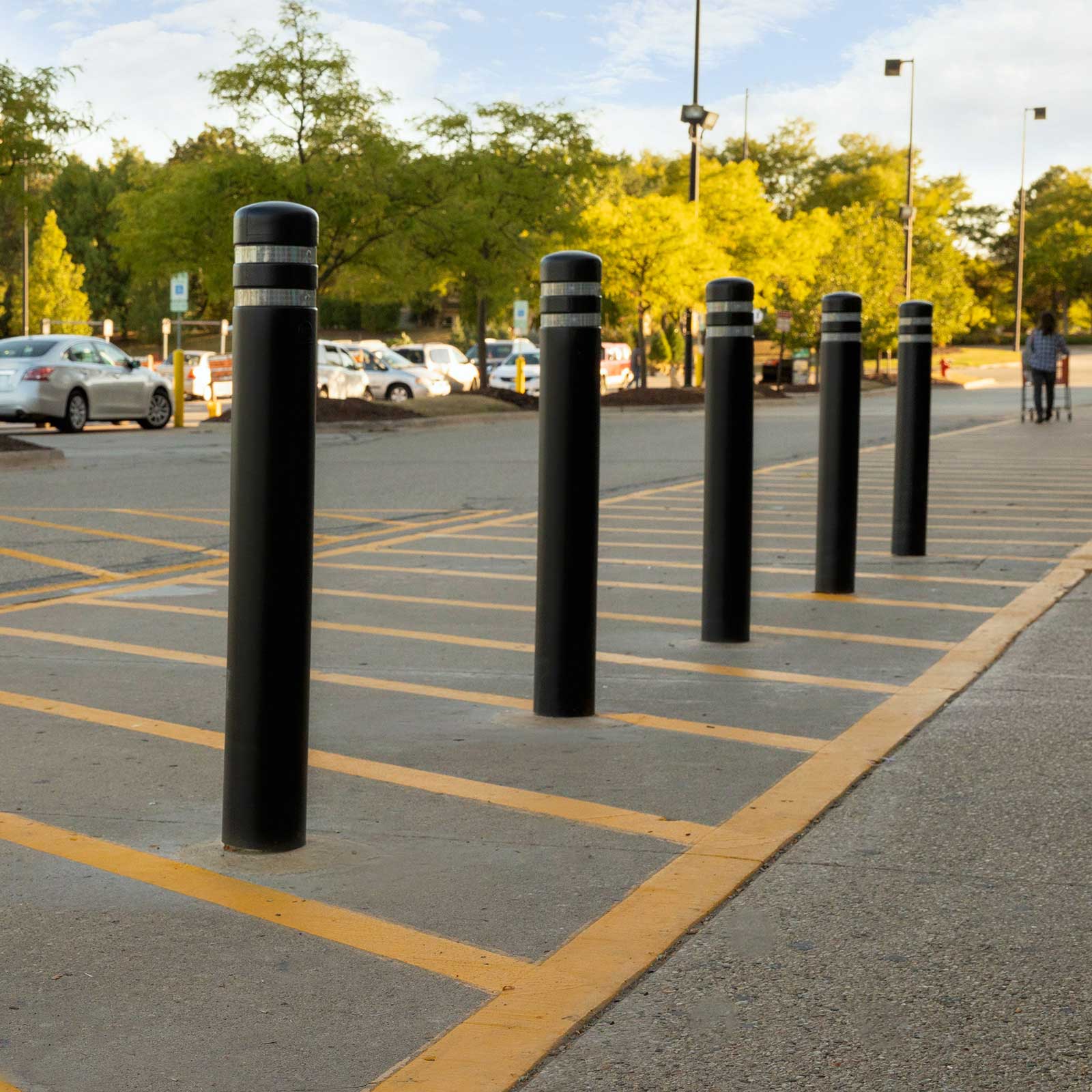 Row of black CrashCore Bollard S10 parking lot safety bollards protecting a walkway between striped stalls.