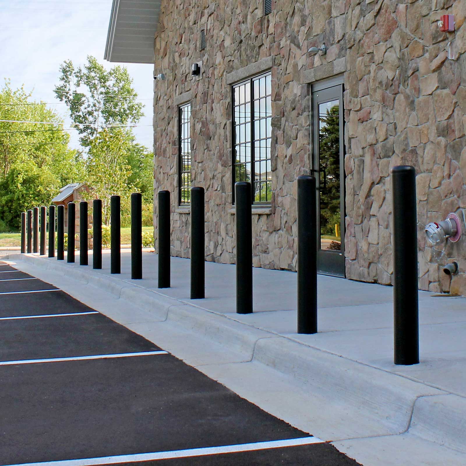 Black CrashCore Bollard S10 bollards along a building sidewalk, protecting pedestrians from nose-in parking.