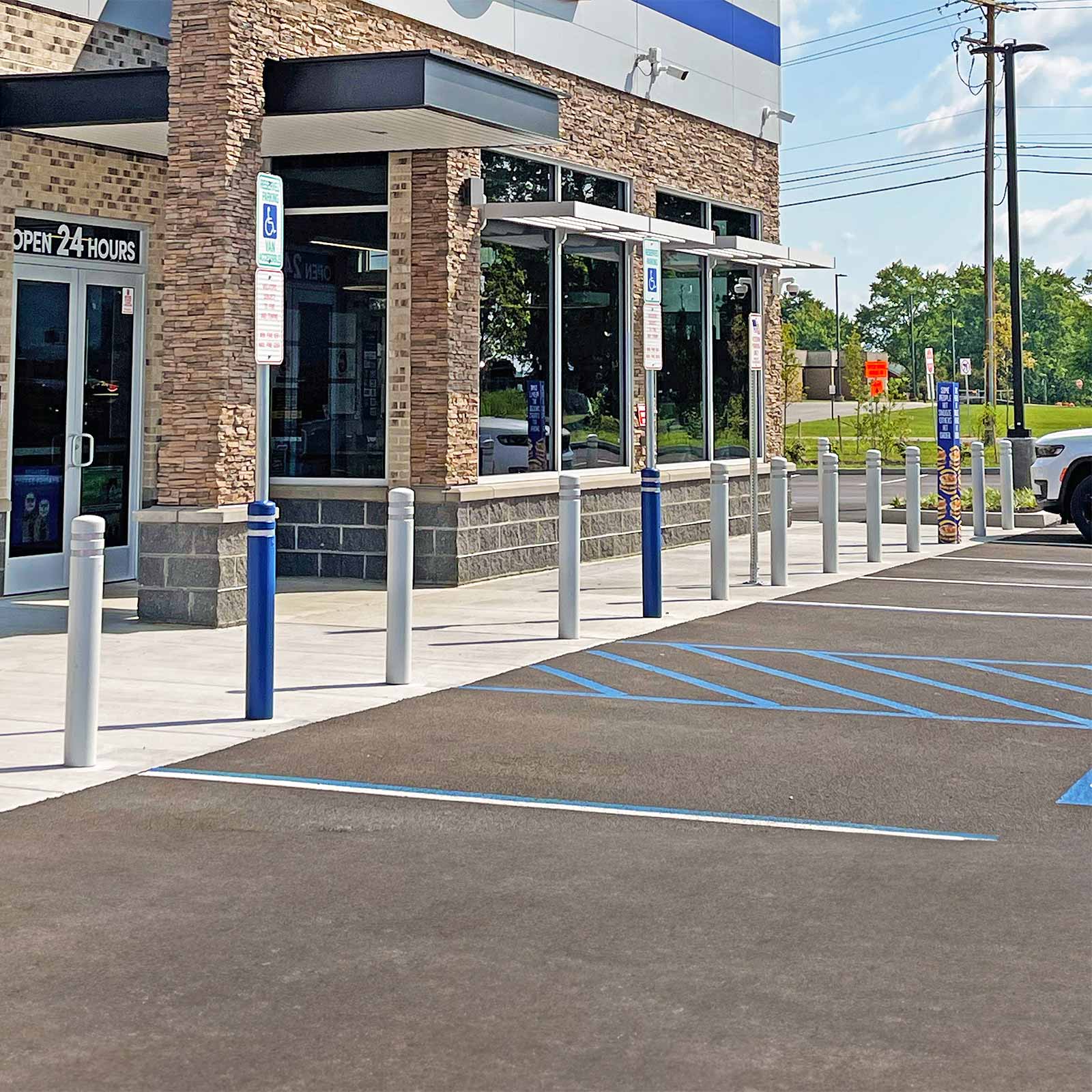 CrashCore Bollard S10 with blue covers and accessible parking signs along a storefront walkway beside a parking lot.