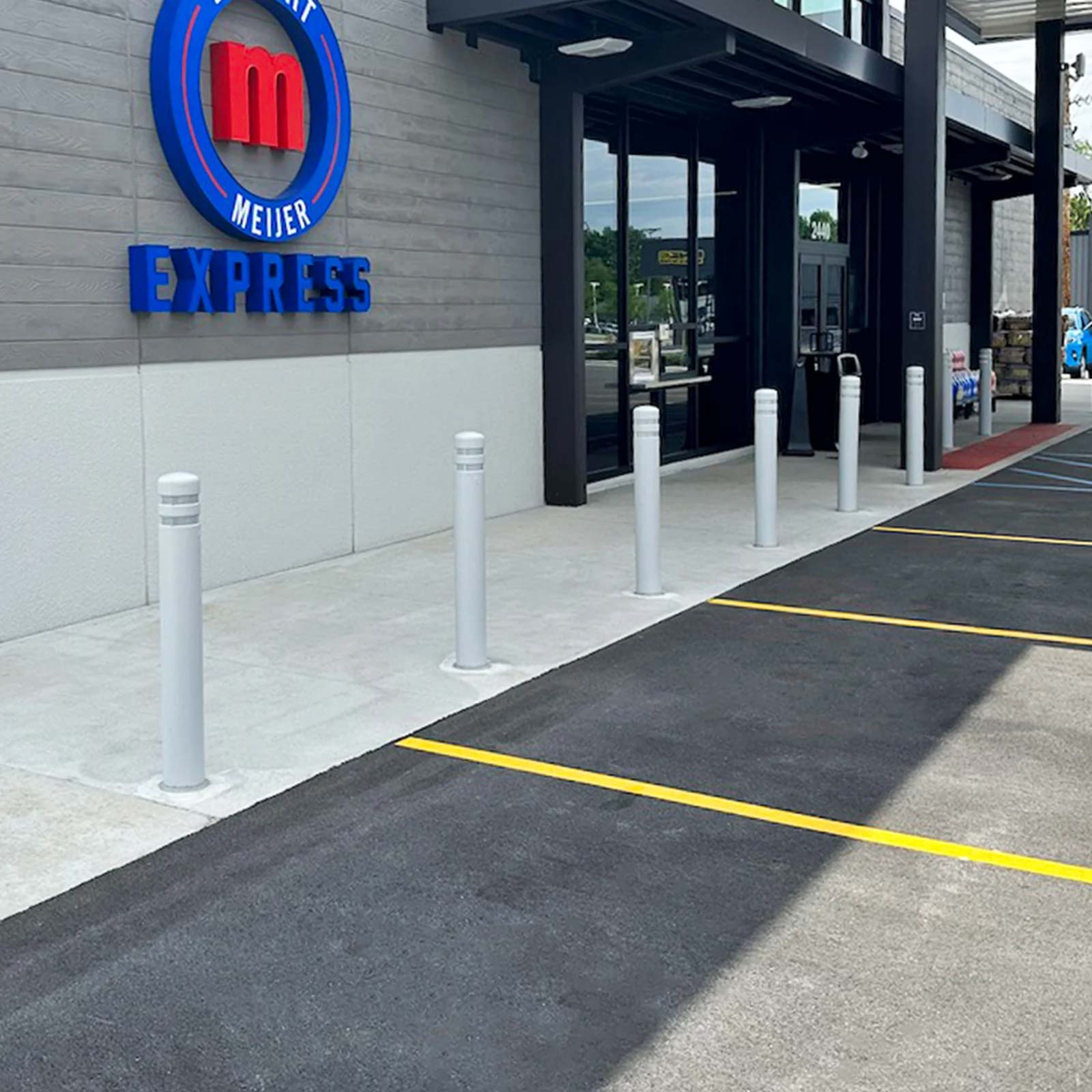 CrashCore Bollard S10 pedestrian protection bollards lining a convenience store entrance beside a no-parking zone.