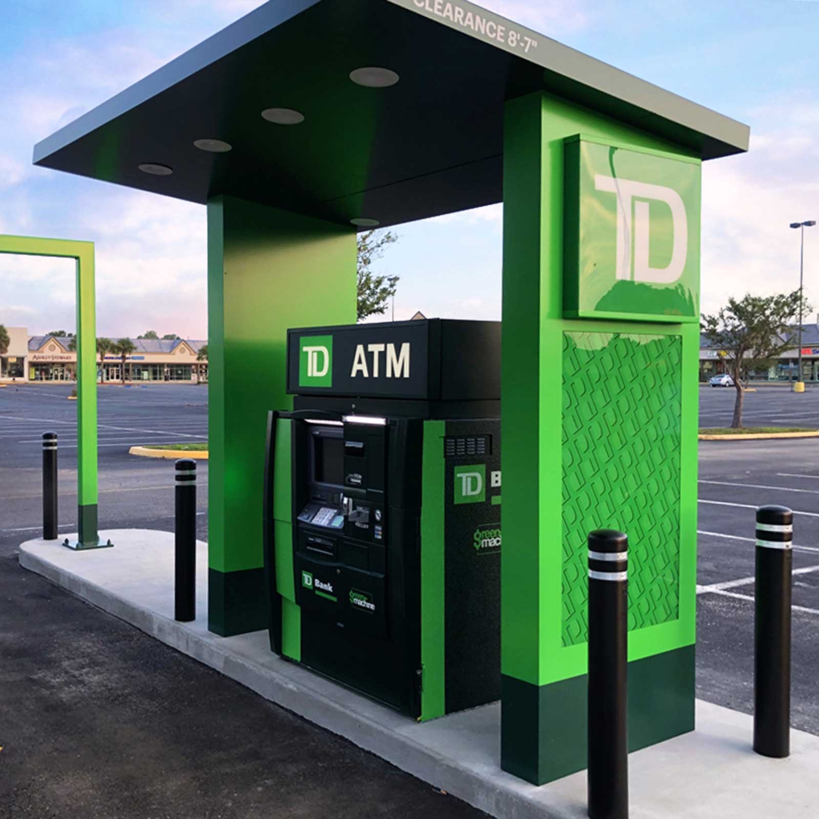 CrashCore Bollard S10 bollards guarding a drive-up ATM kiosk from vehicles in a bank parking lot.