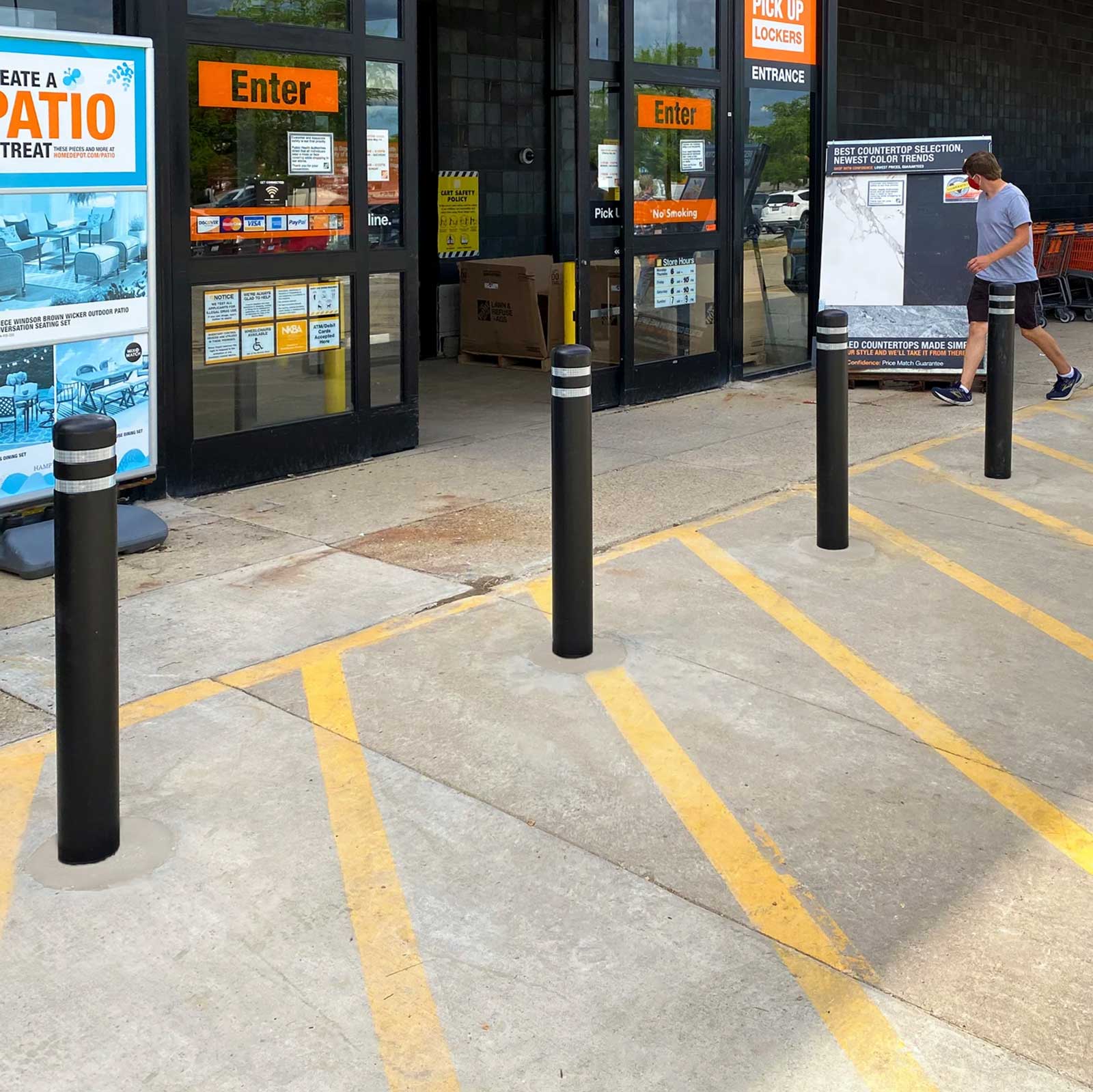CrashCore Bollard S10 storefront crash protection bollards at a home improvement store entrance as a shopper walks in.