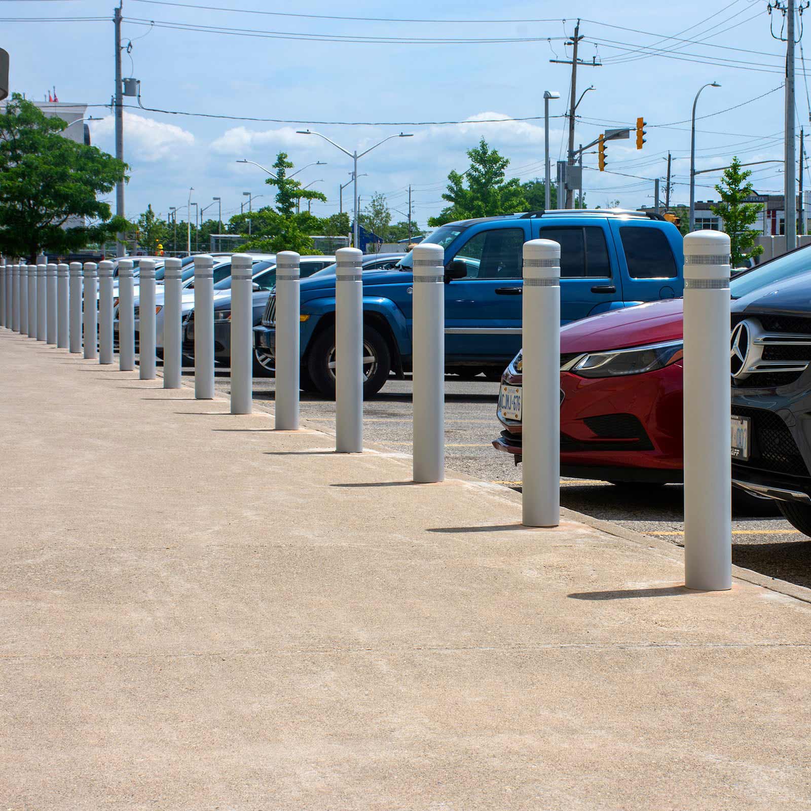Row of Grey CrashCore Bollard S15 parking lot safety bollards along a curb with nose-in parked cars.