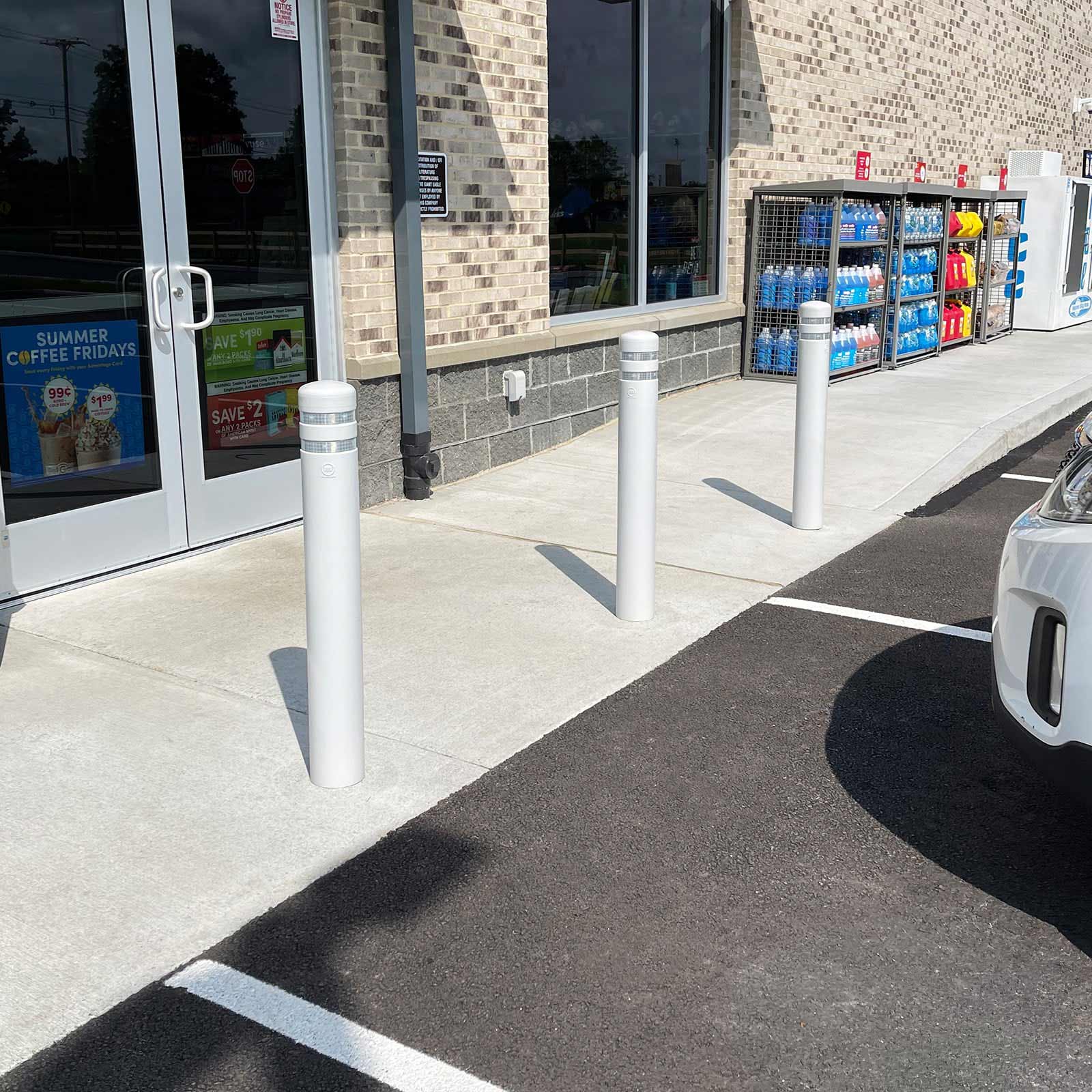 Grey CrashCore Bollard S15 bollards lining a retail storefront sidewalk beside nose-in parking.