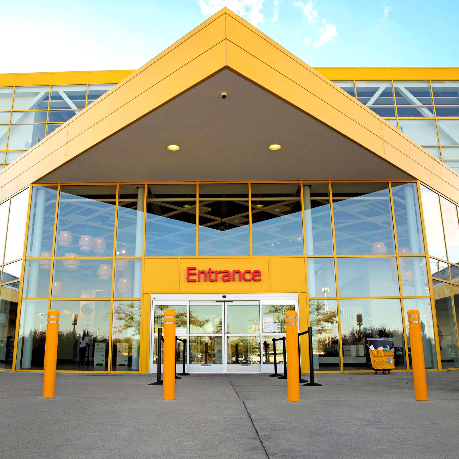Yellow CrashCore Bollard S15 crash bollards guarding the entrance of a commercial building.