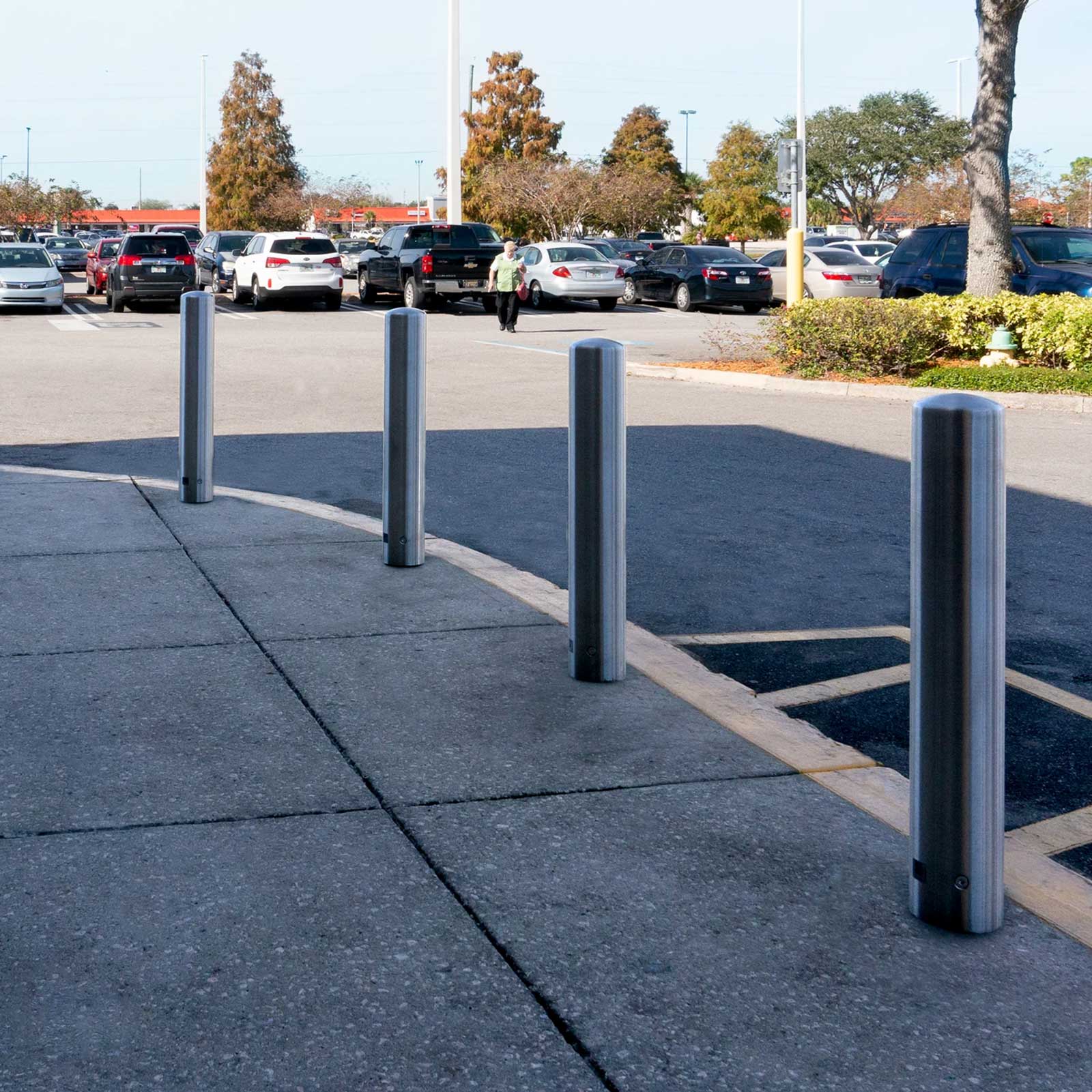 Stainless Steel CrashCore Bollard S20 bollards along a sidewalk, separating the building perimeter from a busy parking lot.