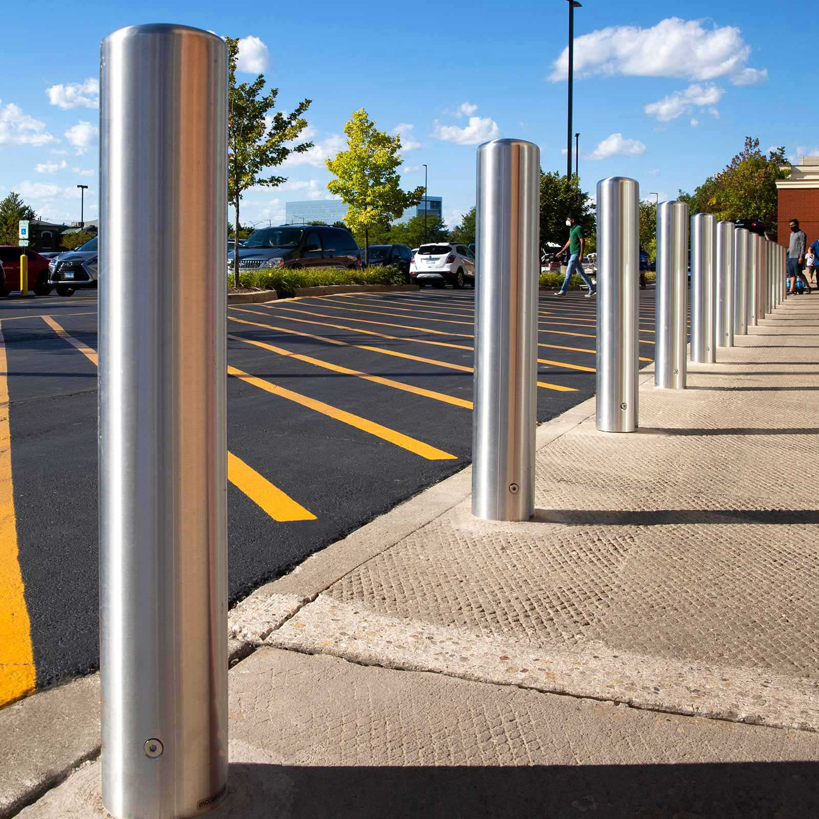 Stainless Steel CrashCore Bollard S20 crash-tested bollards lining a storefront curb between the parking lot and the walkway.