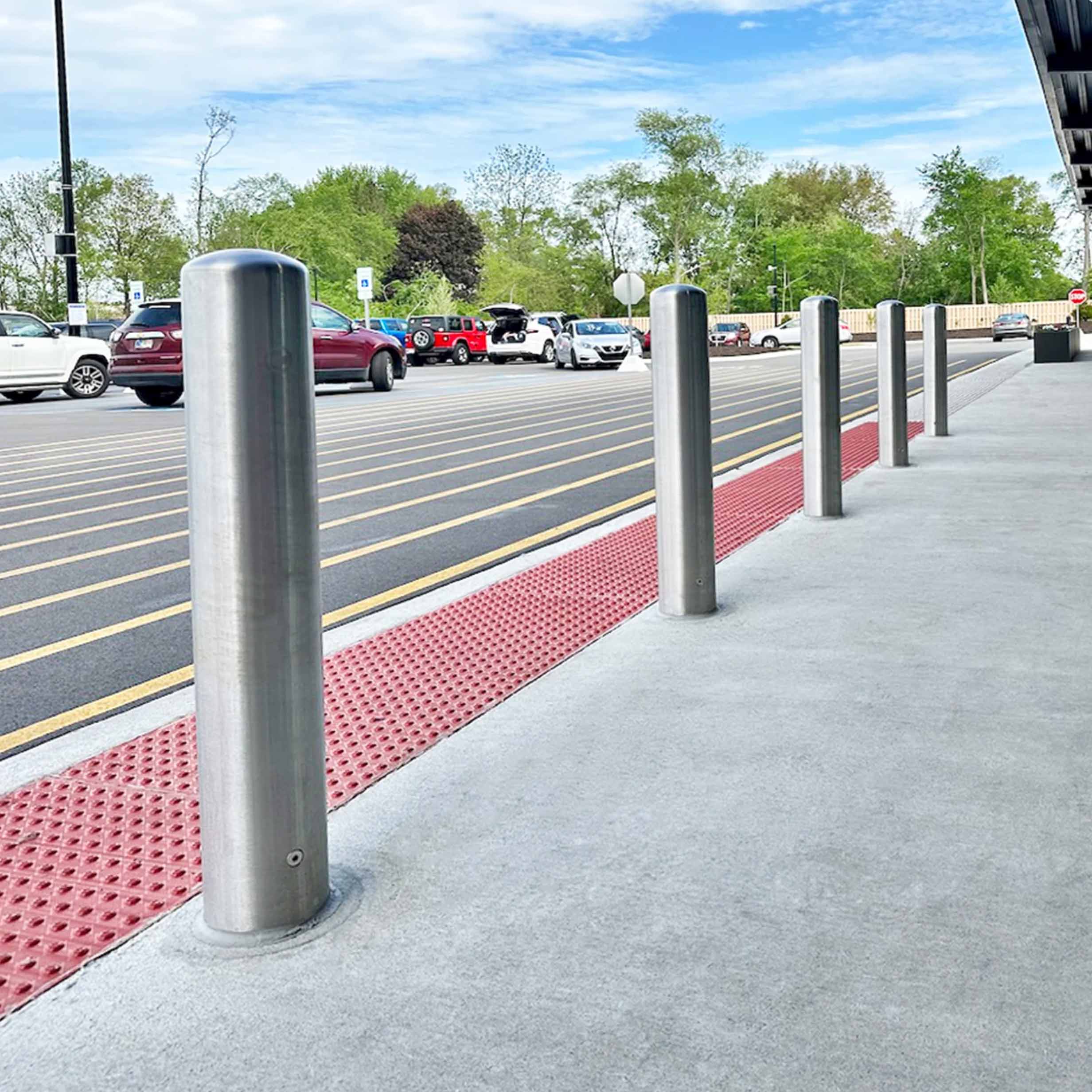 Row of stainless CrashCore Bollard S20 bollards protecting a storefront walkway from nose-in parking.